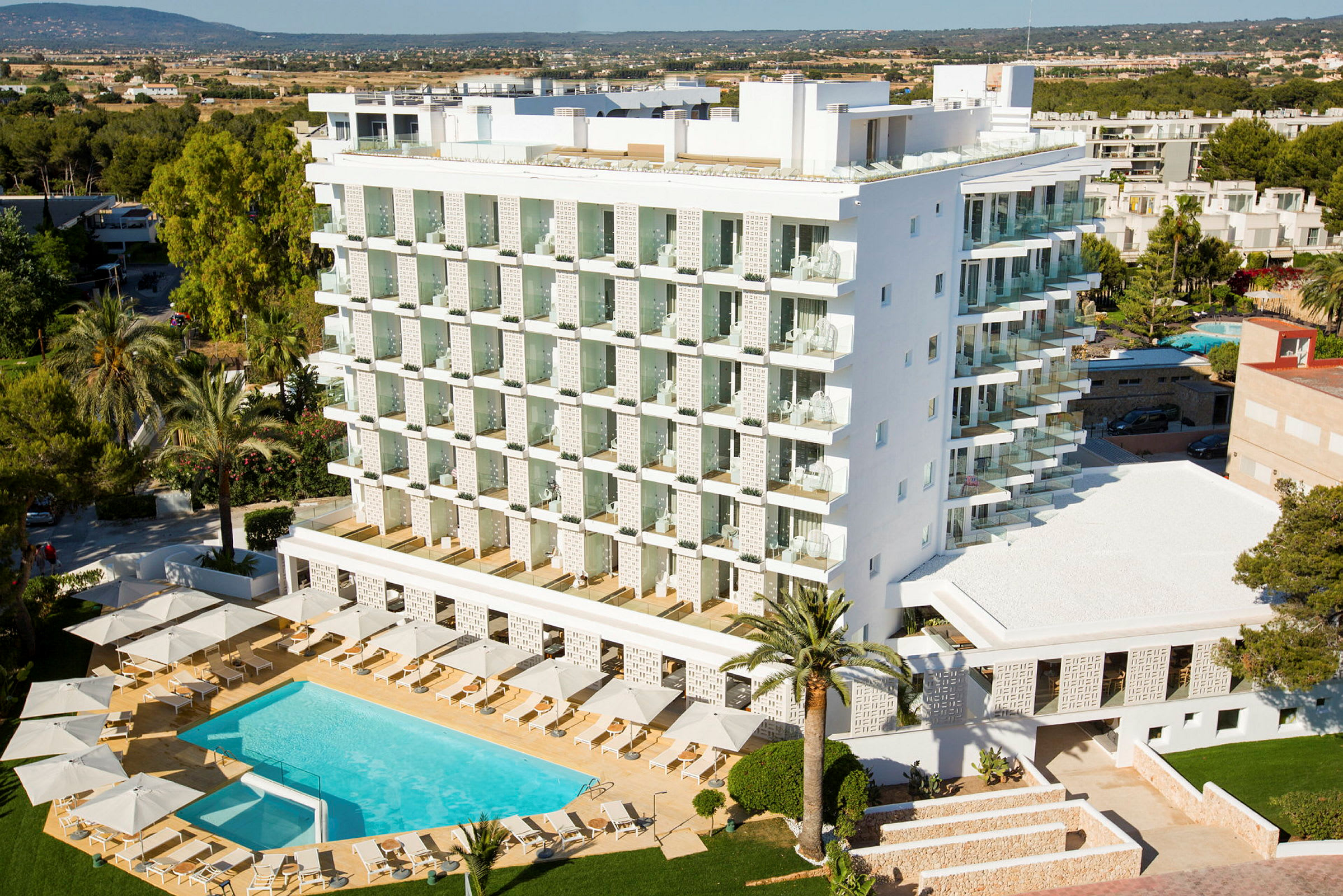 En moderne hotelbygning med en pool og liggestole omkring den, omgivet af træer og grønne områder. (AI-genereret tekst)