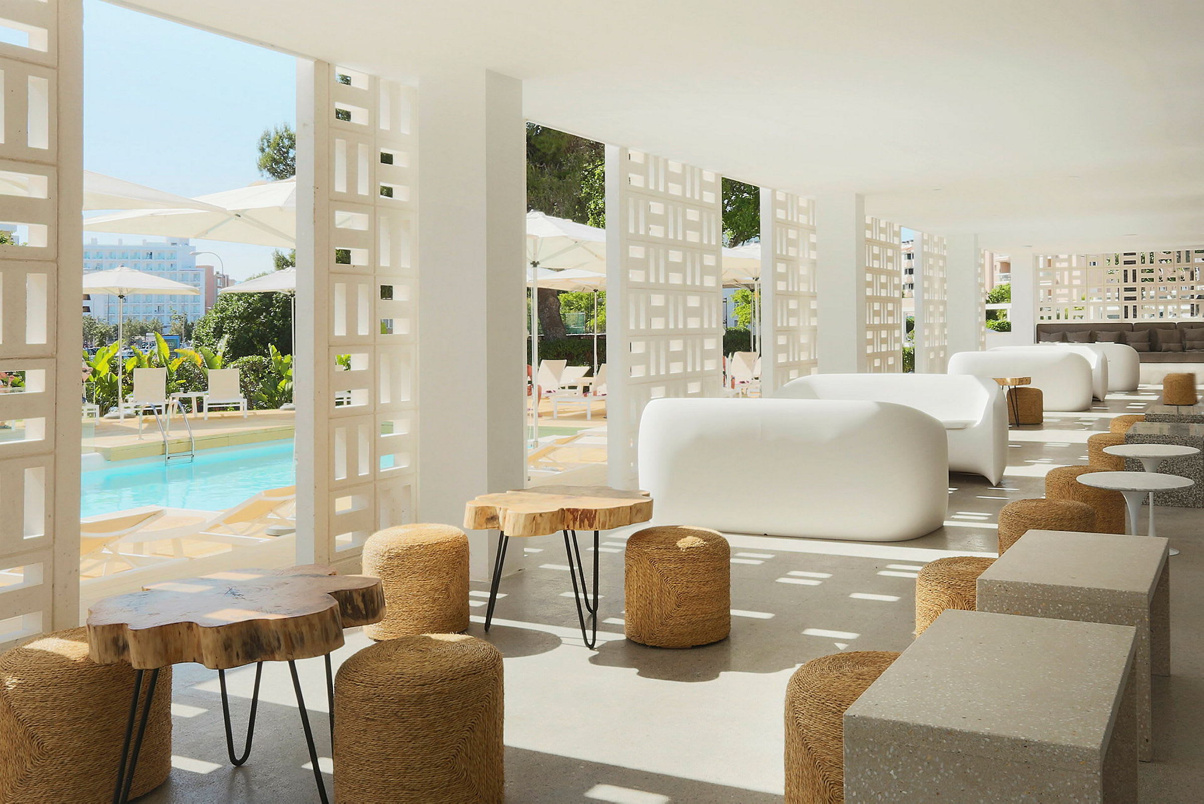 Moderne lounge med hvide sofaer og træborde, med udsigt over en pool og parasoller. (AI-genereret tekst)