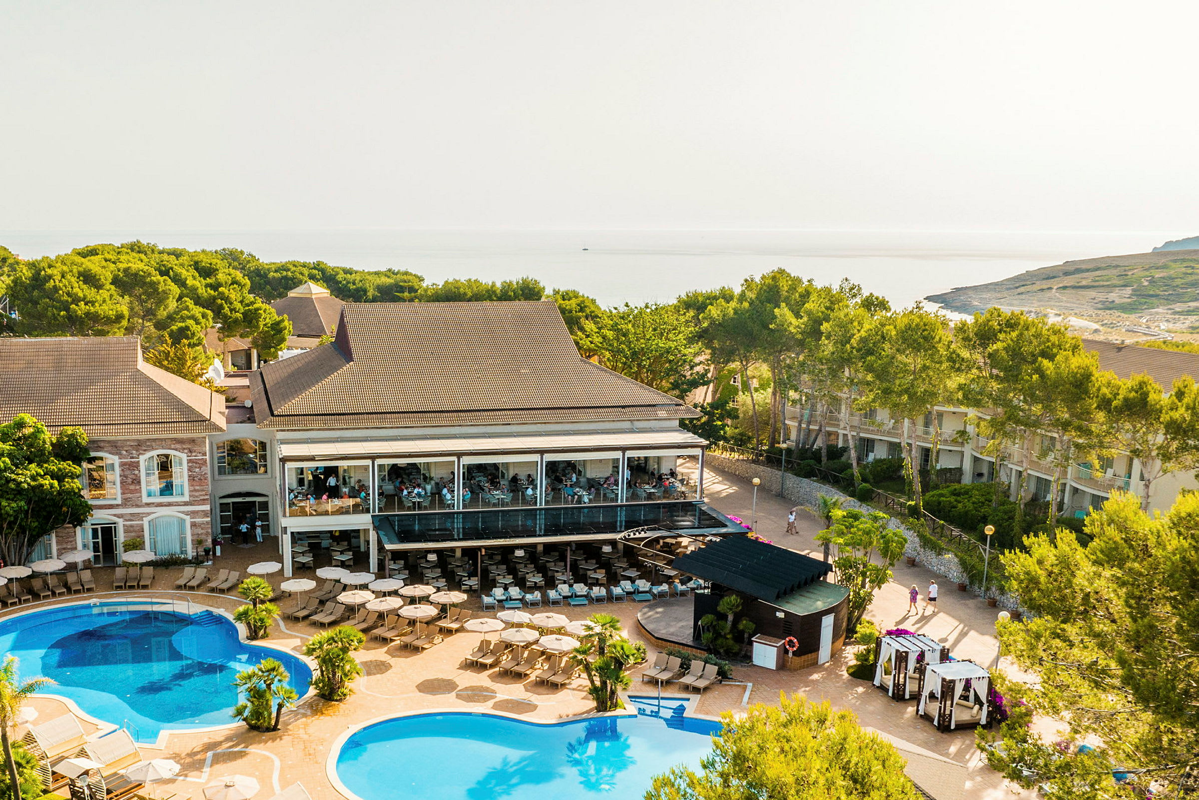 Billede af en resort med flere bygninger, swimmingpools og omkringliggende grønne områder. (AI-genereret tekst)