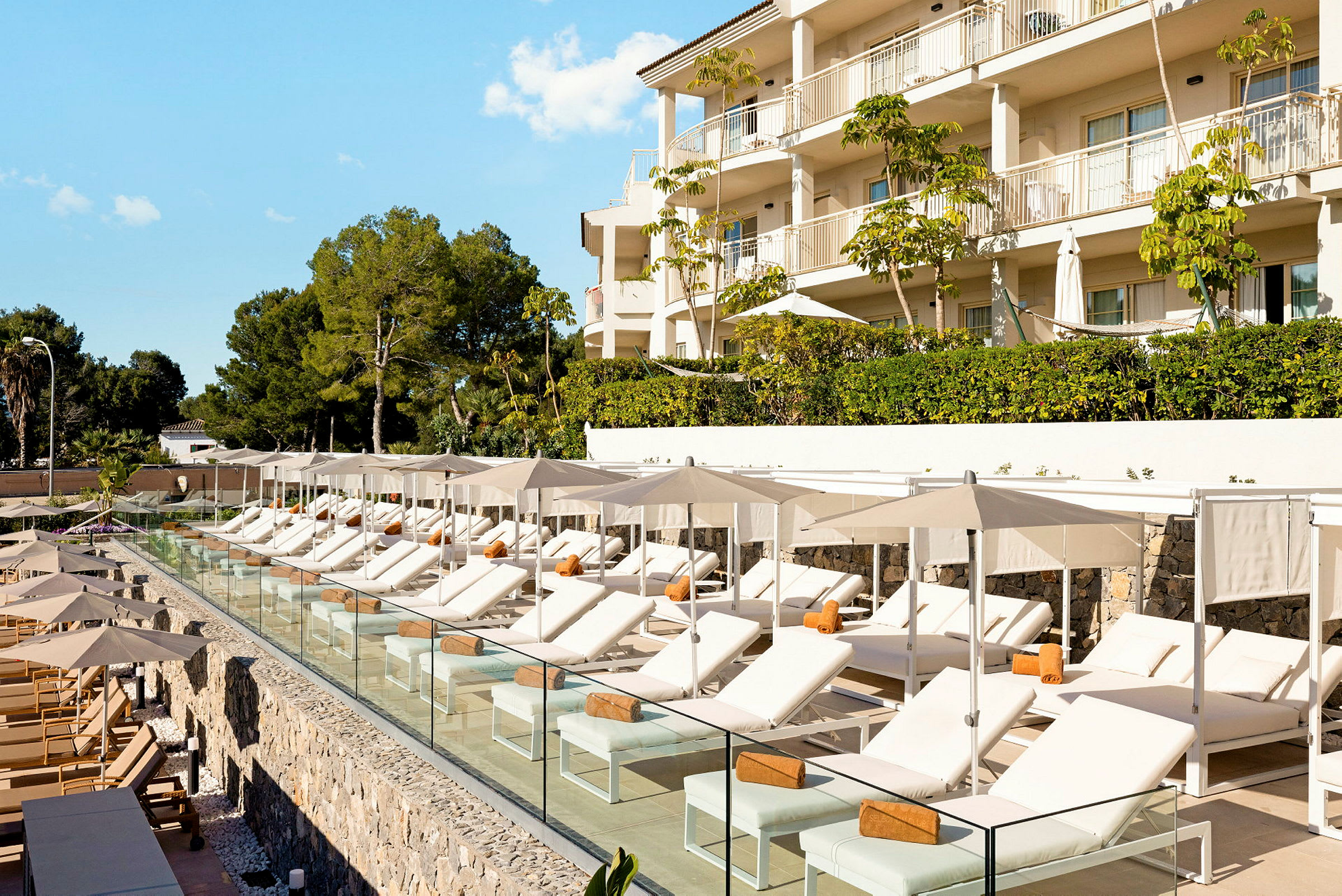 Liggestole med parasoller ved en pool tæt på et hotel. (AI-genereret tekst)