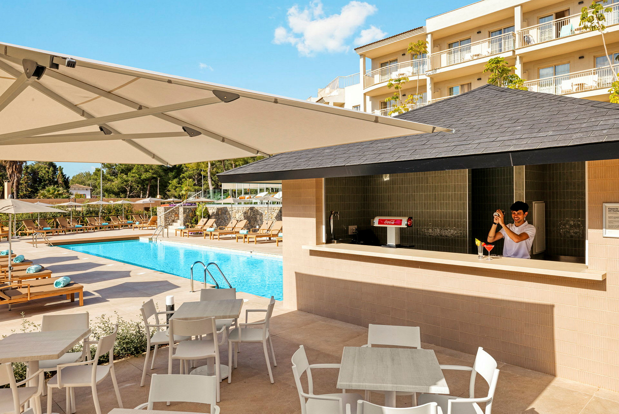 Billedet viser en udendørs swimmingpool omgivet af liggestole og parasoller, med en bar i forgrunden. (AI-genereret tekst)