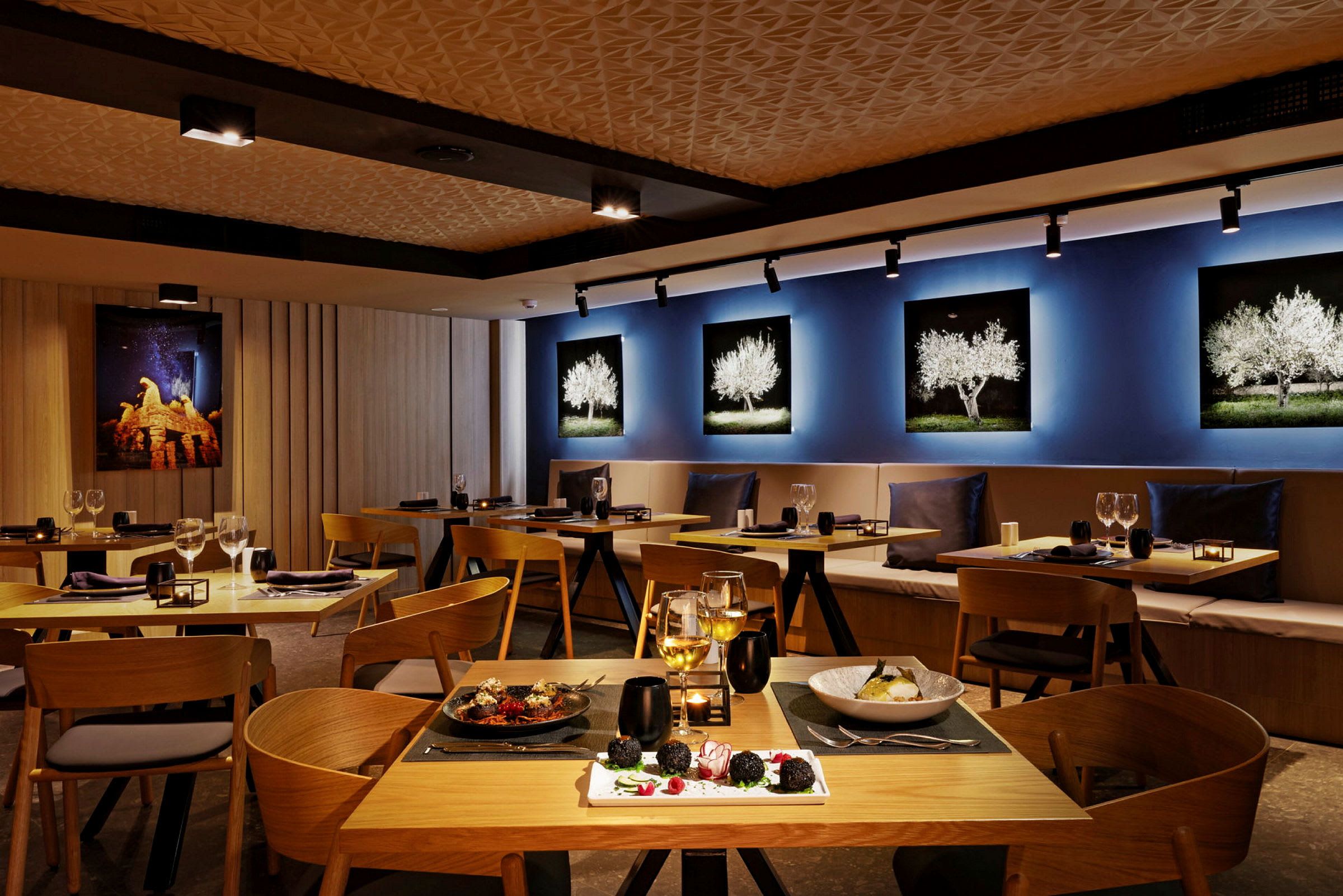 Interiør af en restaurant med træborde og stole, dekorative vægbilleder og serveret mad på bordene. (AI-genereret tekst)