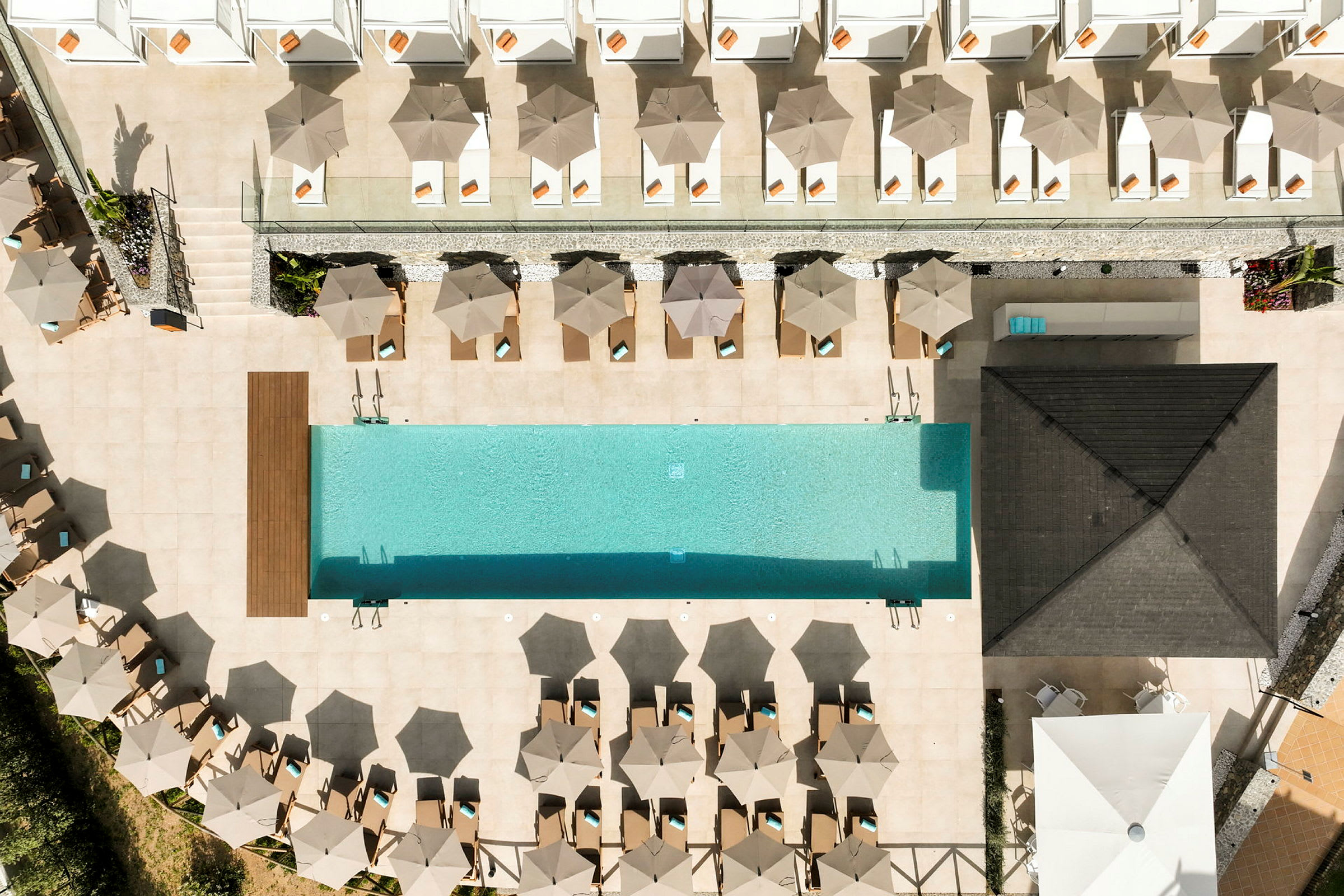 Luftfoto af en rektangulær pool med liggestole og parasoller omkring. (AI-genereret tekst)