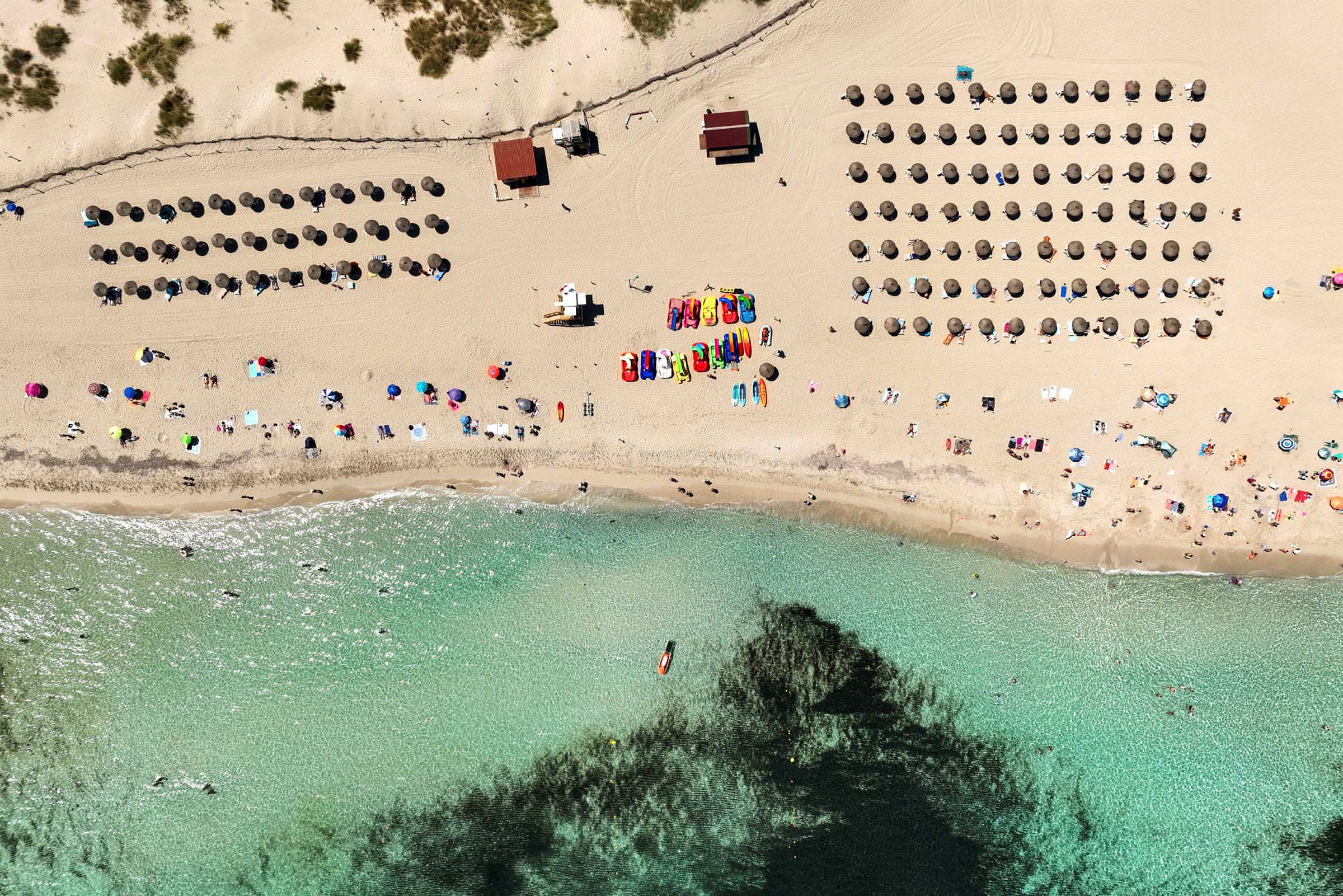 Luftfoto af en strand med parasoller, mennesker og klart vand. (AI-genereret tekst)