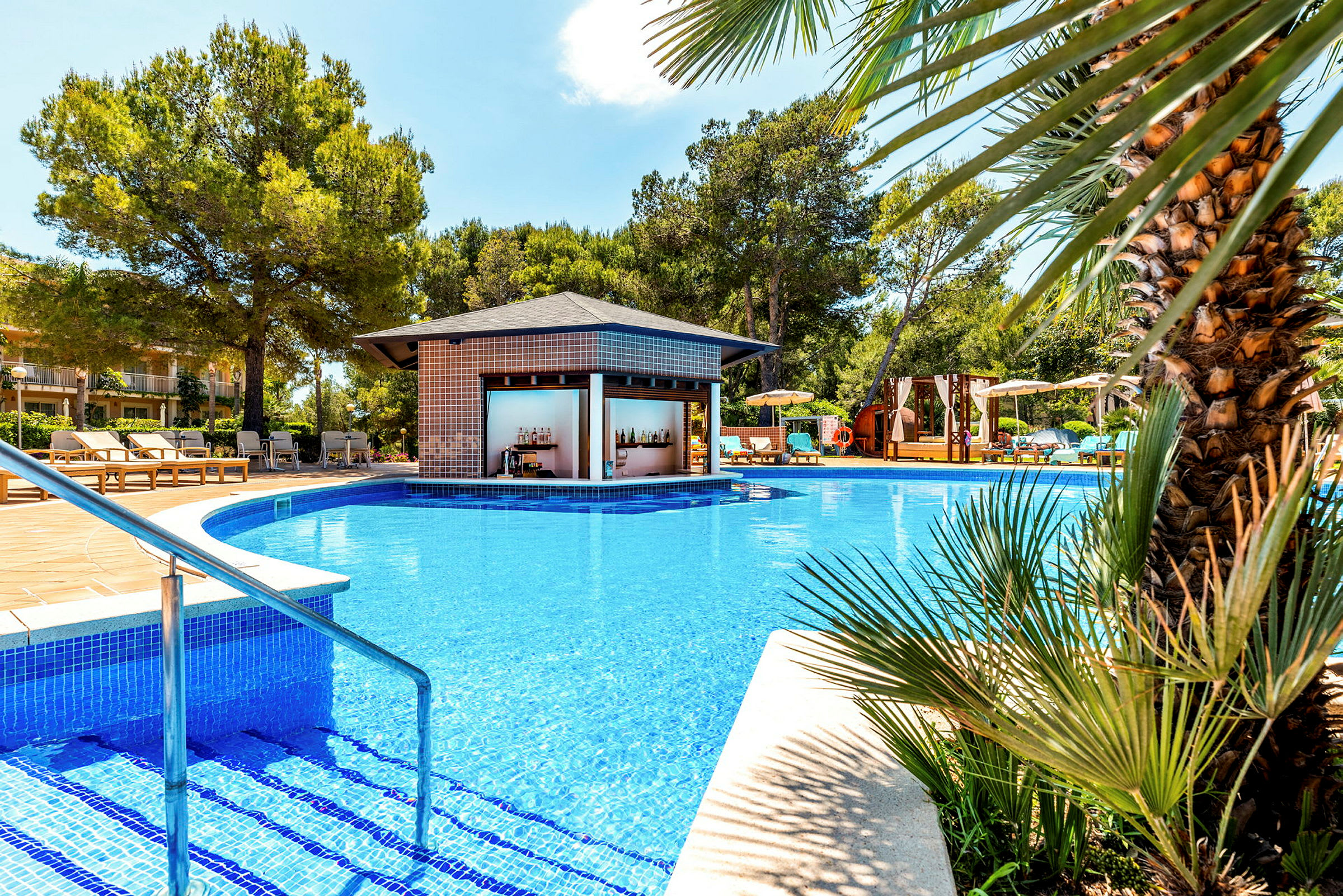Udendørs swimmingpool med træer og en poolbar i baggrunden. (AI-genereret tekst)