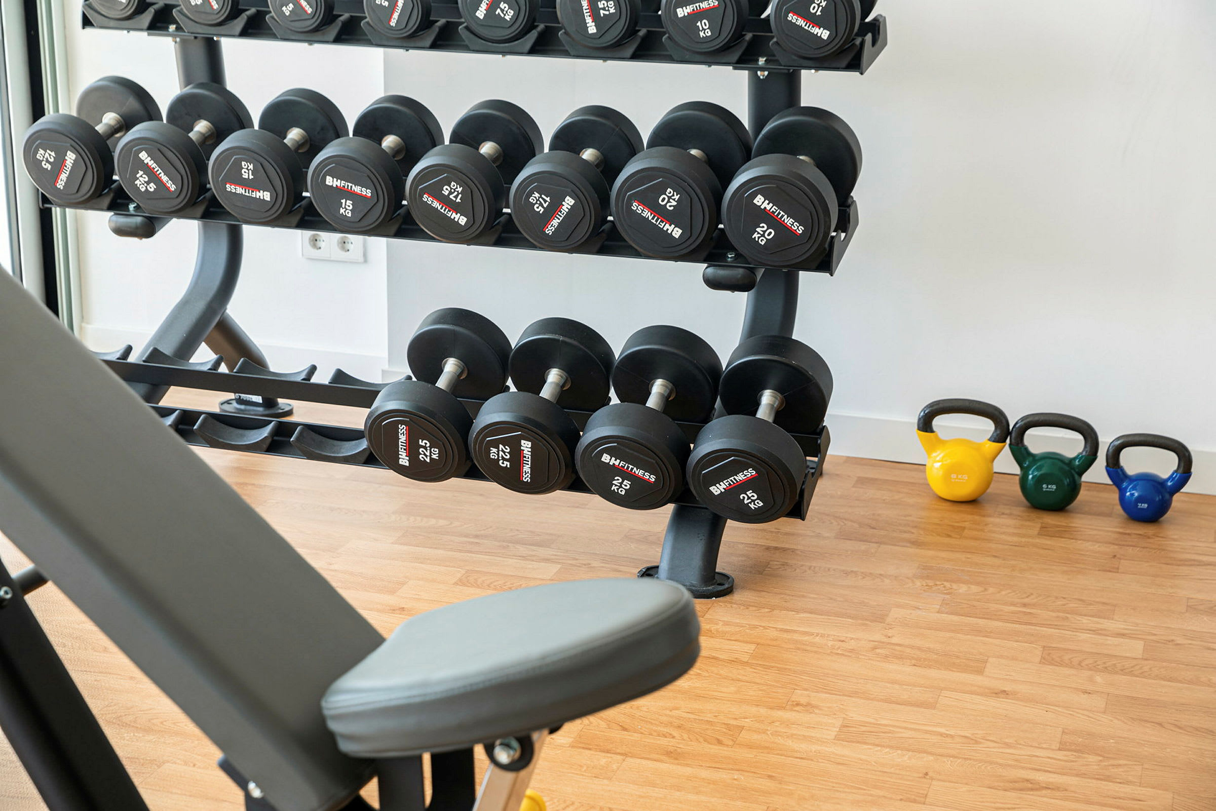 Gymudstyr med håndvægte og kettlebells på et trægulv. (AI-genereret tekst)