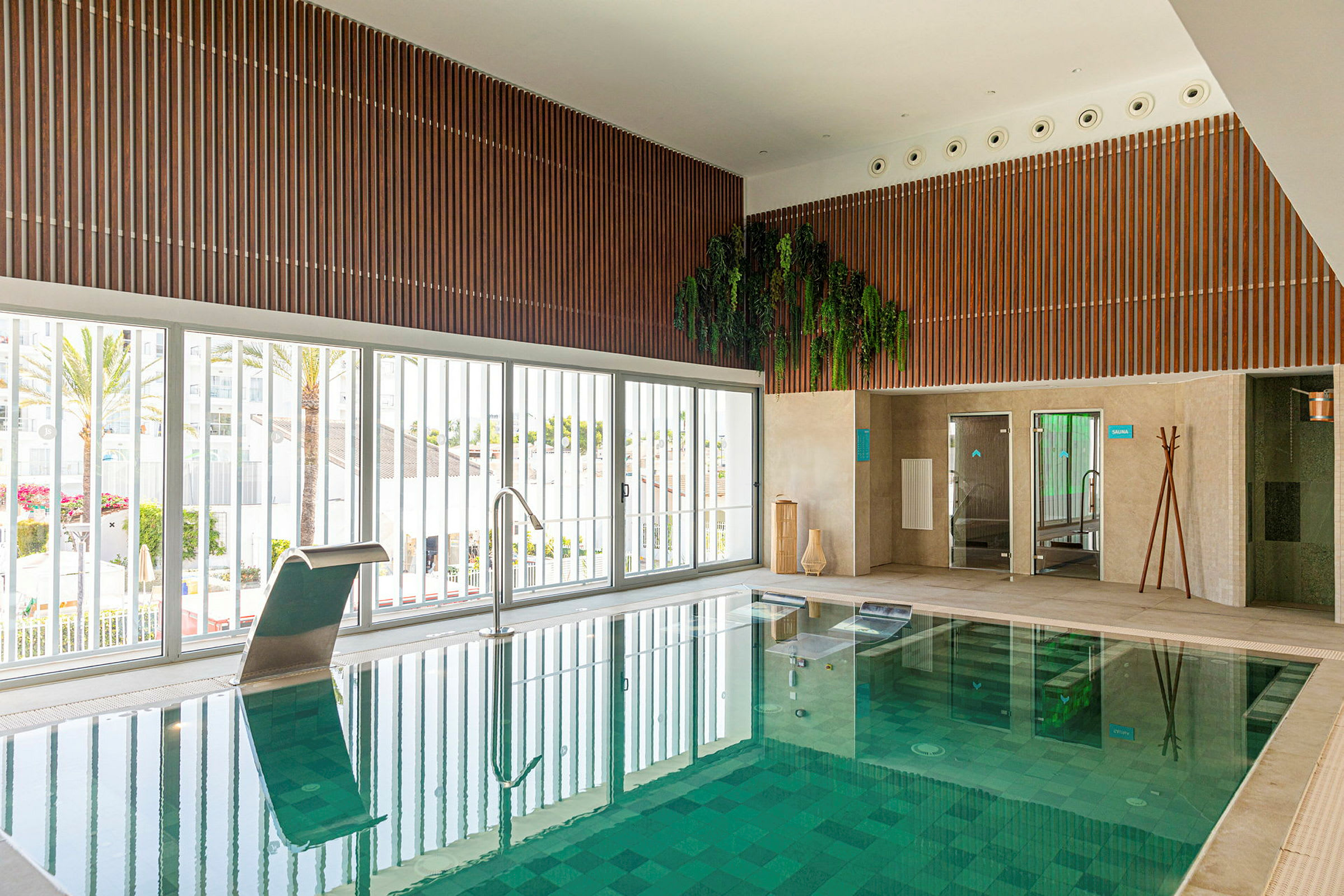 Indendørs pool med grøn mosaik omgivet af store vinduer og vægpaneler i træ. (AI-genereret tekst)