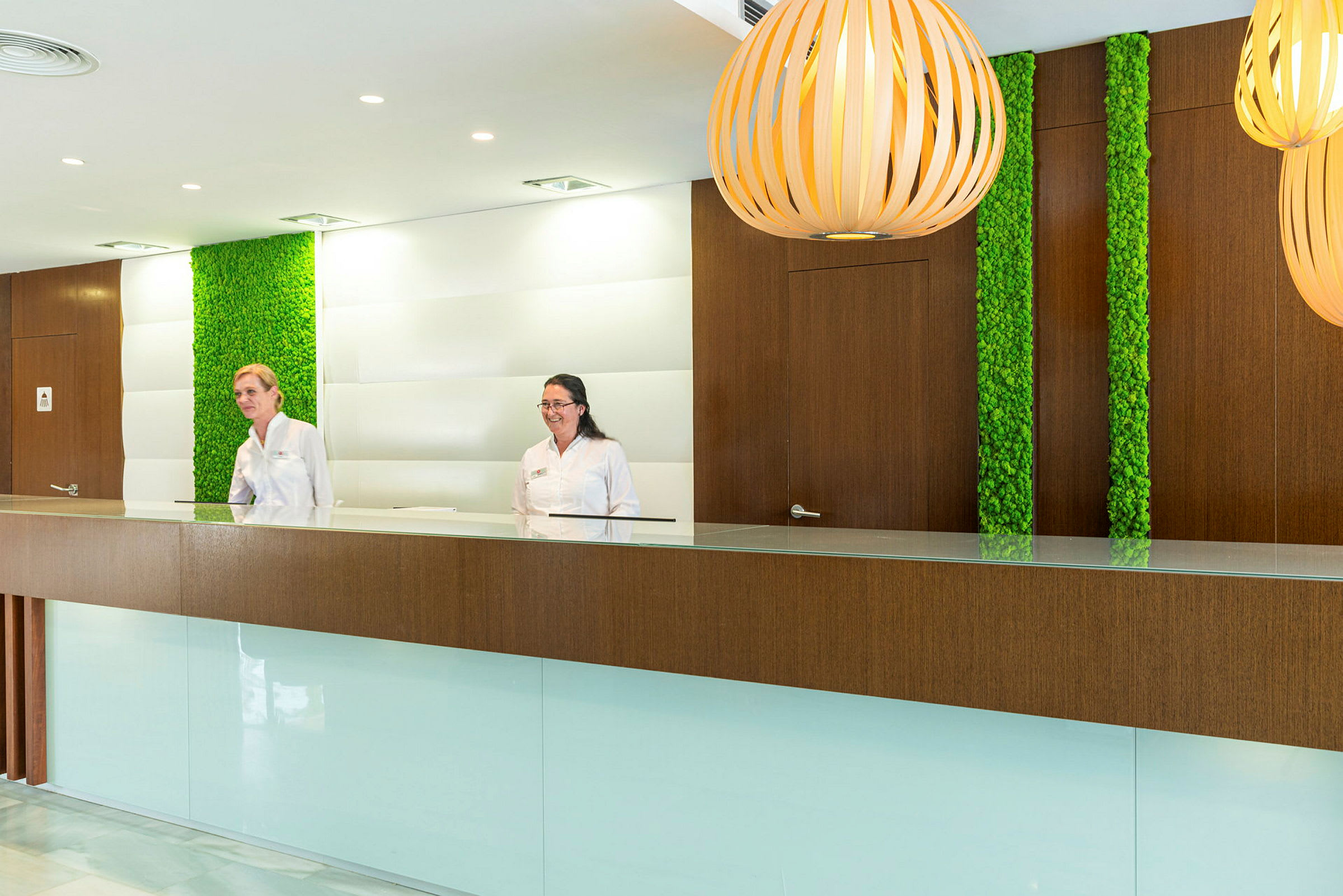 Reception med moderne indretning, herunder detaljer af træ og grønne plantepaneler samt elegante lamper. (AI-genereret tekst)