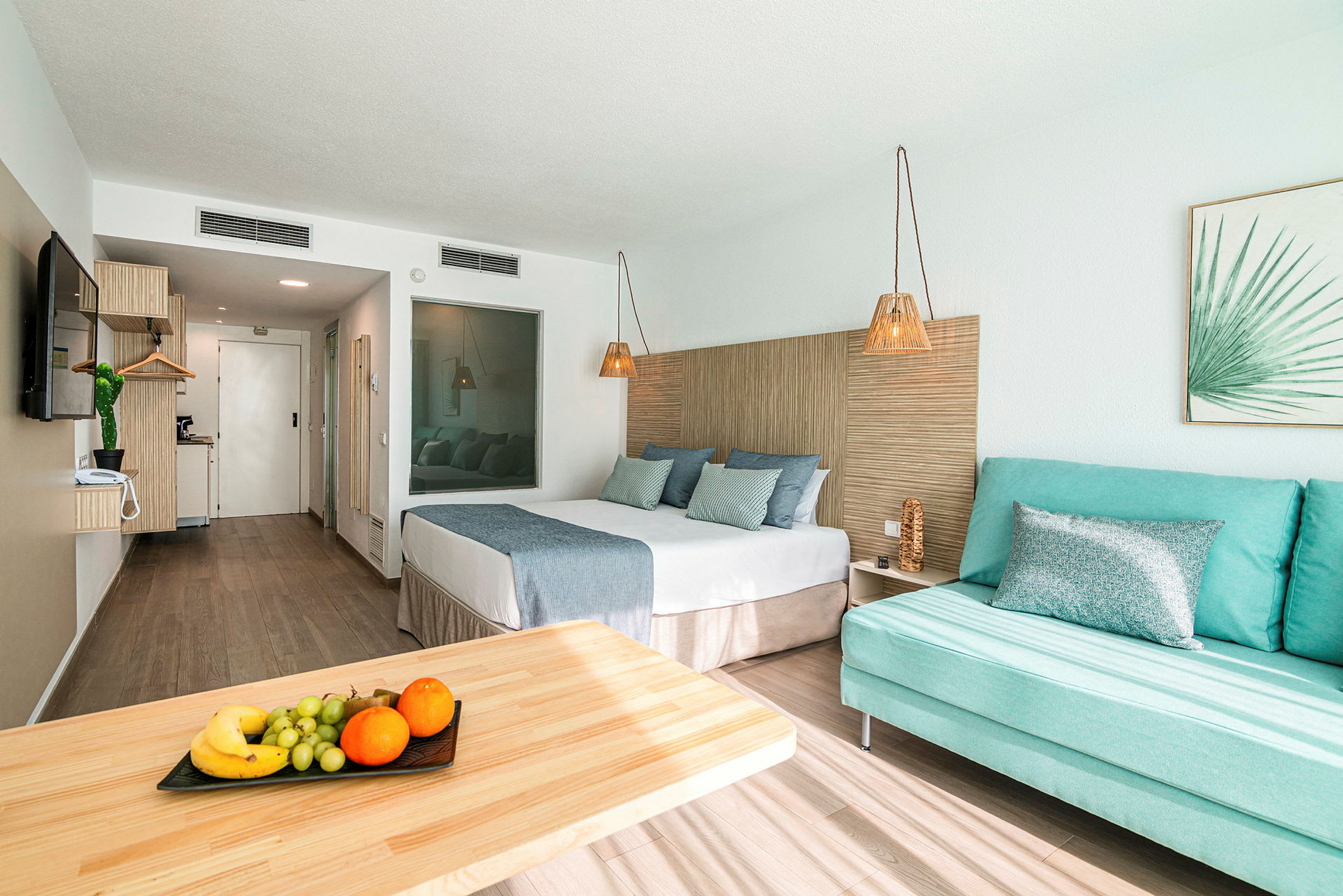 Hotelværelse med seng, sofa og bord med frugt. (AI-genereret tekst)
