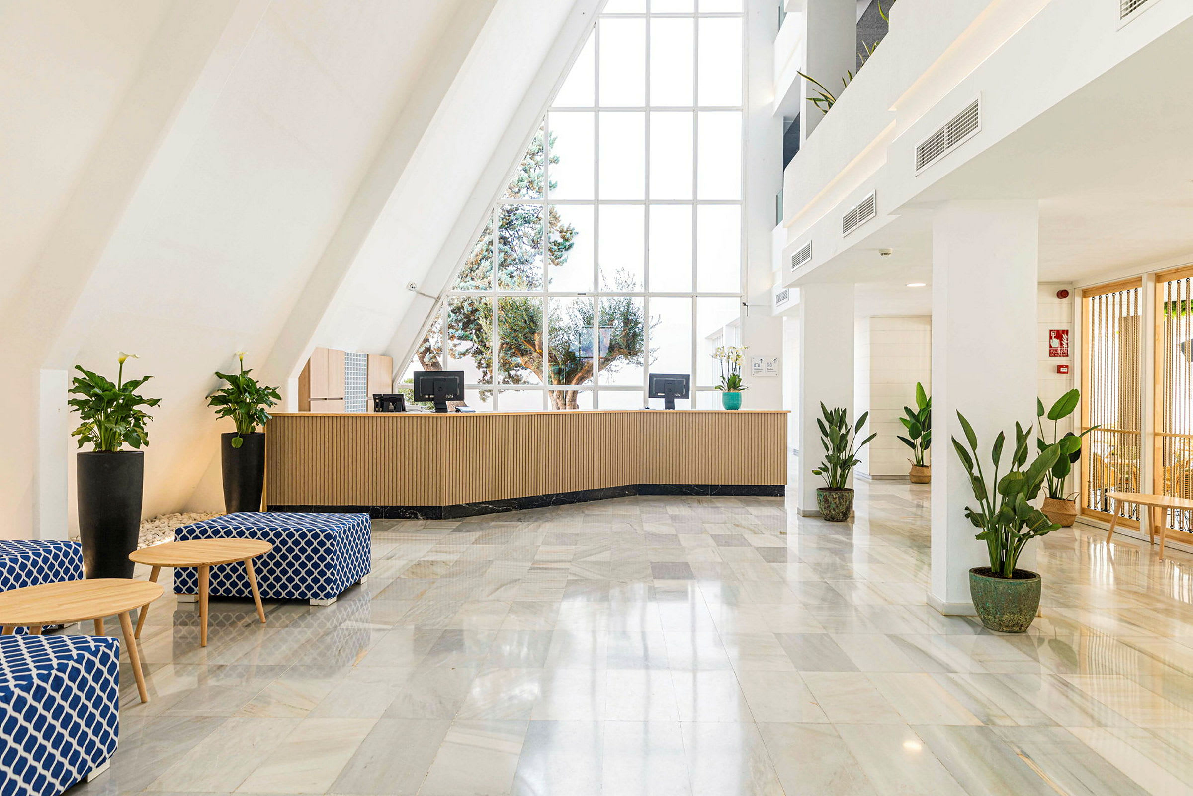 Hotelreception med store vinduer, lænestole og potteplanter. (AI-genereret tekst)