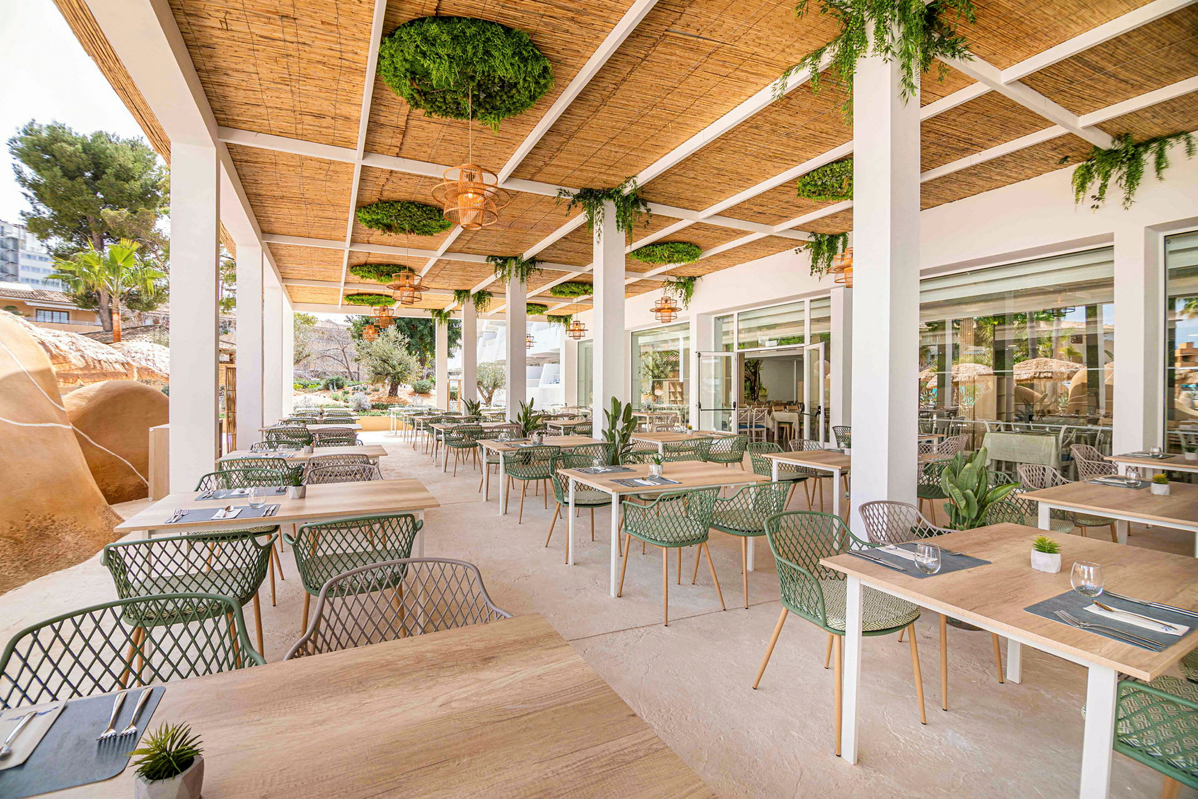 Udendørsrestaurant med borde og stole under et tag med grønne planter. (AI-genereret tekst)