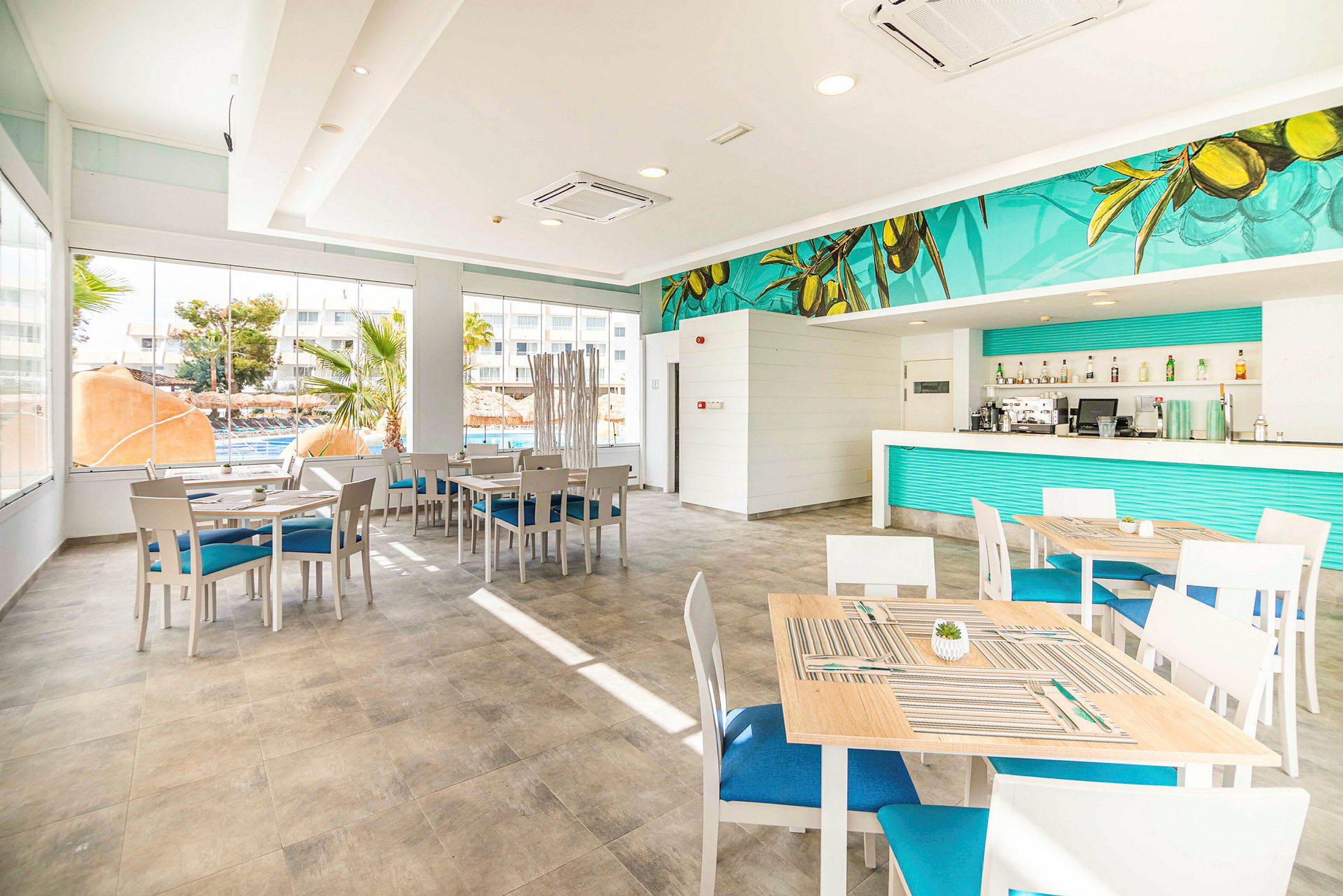 Lyse møbler i en moderne restaurant med blå detaljer og store vinduer. (AI-genereret tekst)