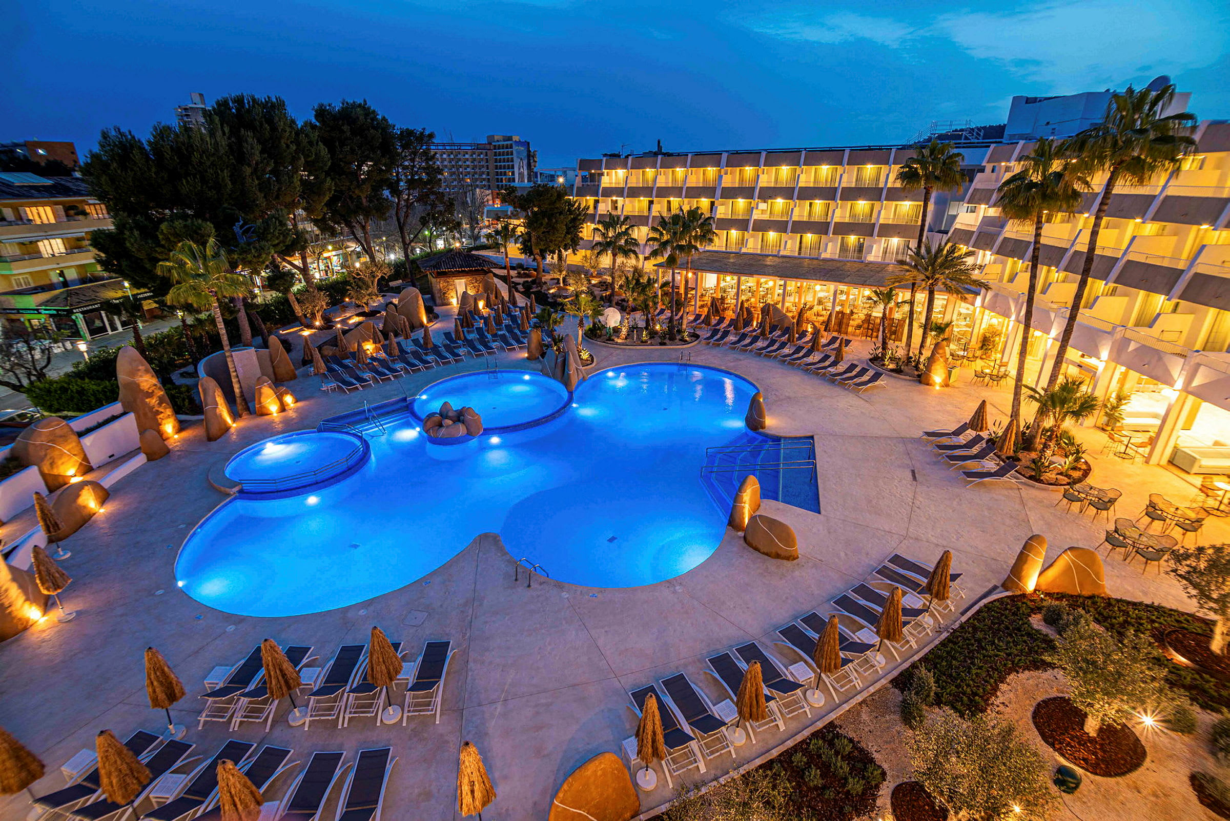 Oplyst hotelområde med pool og liggestole om aftenen. (AI-genereret tekst)