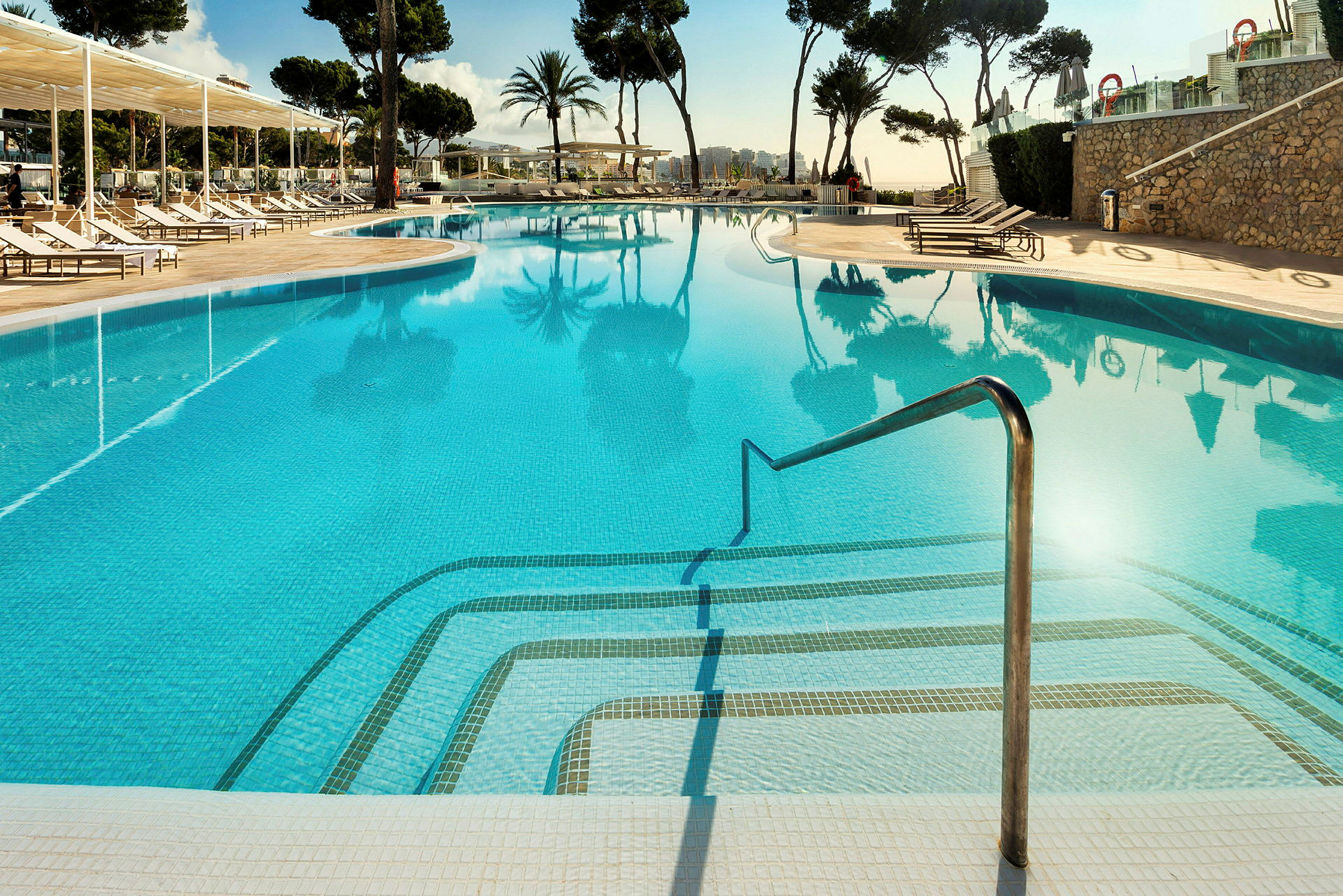 Udendørs swimmingpool med klart vand, omgivet af liggestole og parasoller. (AI-genereret tekst)