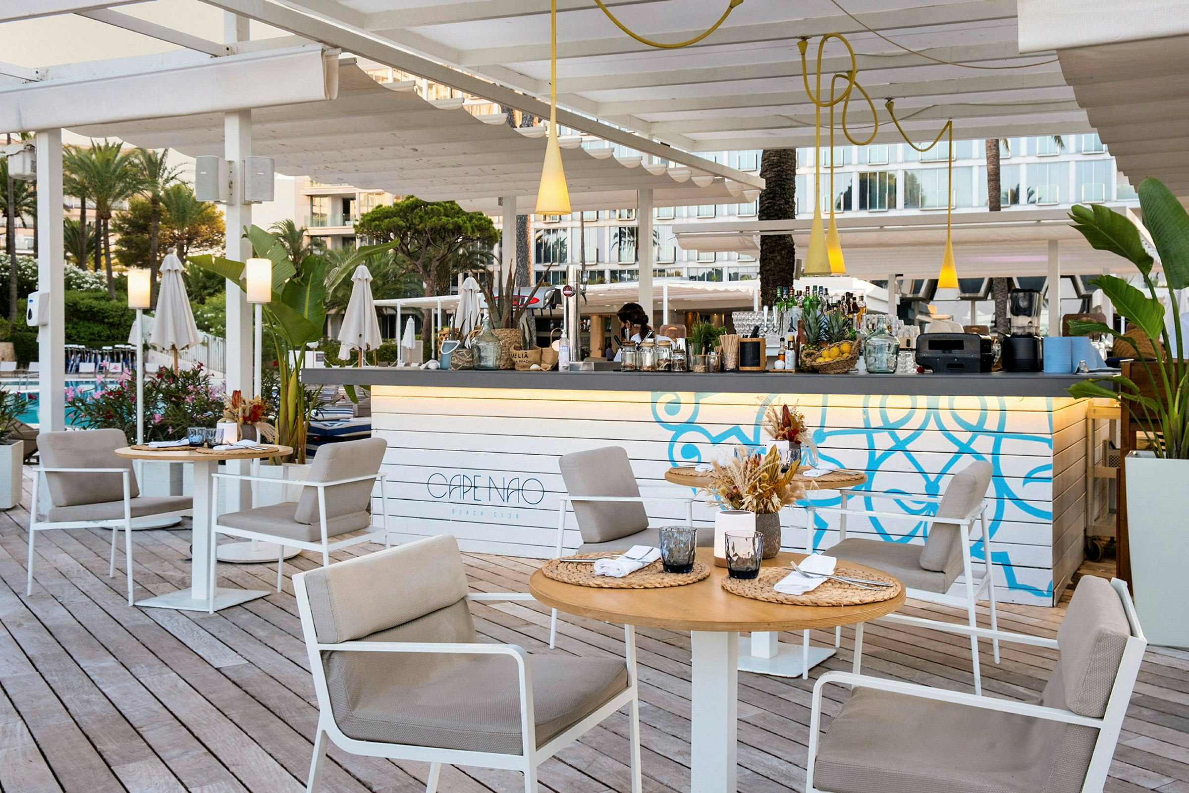 Udendørsmiljø ved en strandklub med siddegrupper, et dekorativt barområde og grønne planter. (AI-genereret tekst)