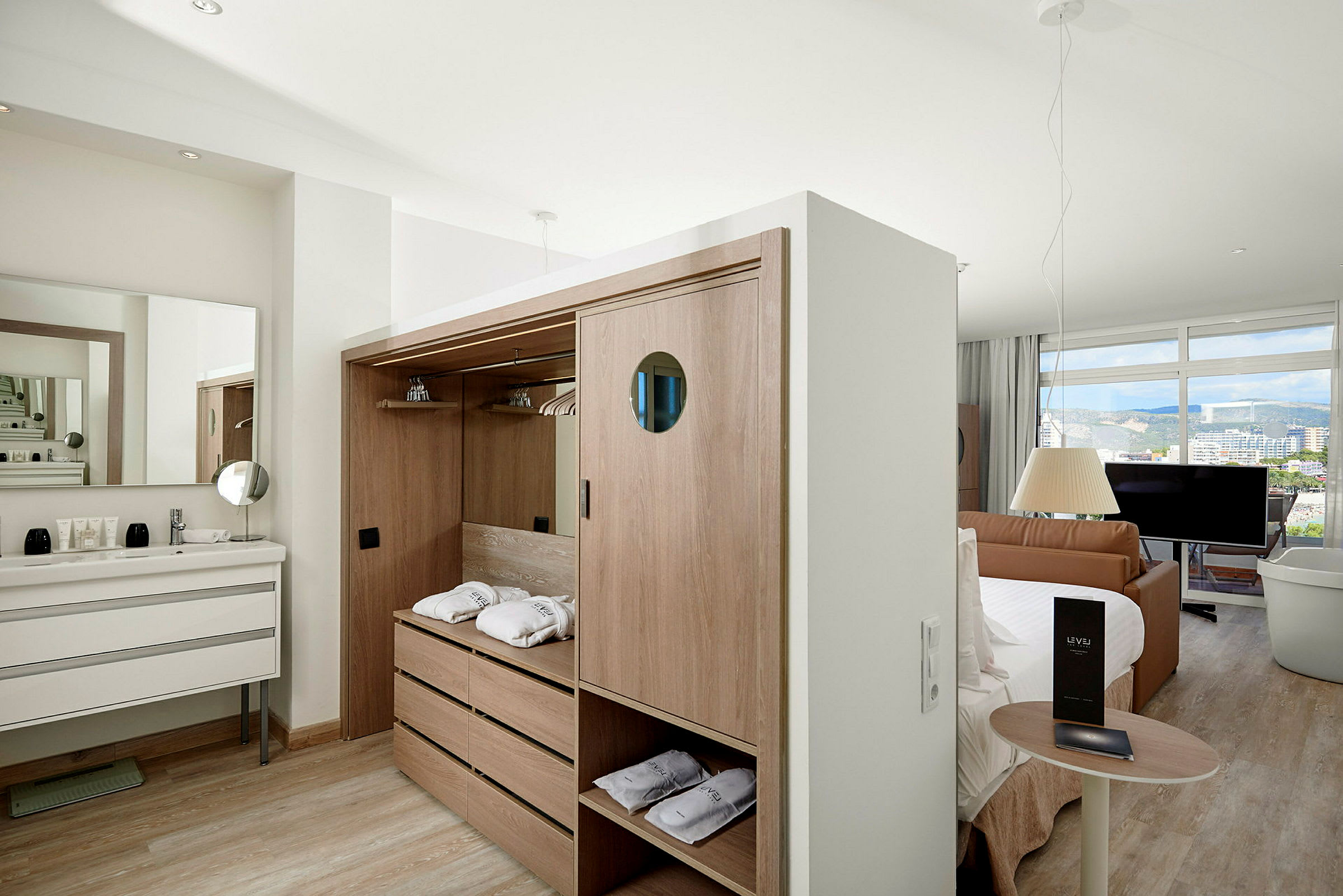 Et hotelværelse med garderobe, håndvask, seng, sofa og en stor vinduesudsigt. (AI-genereret tekst)