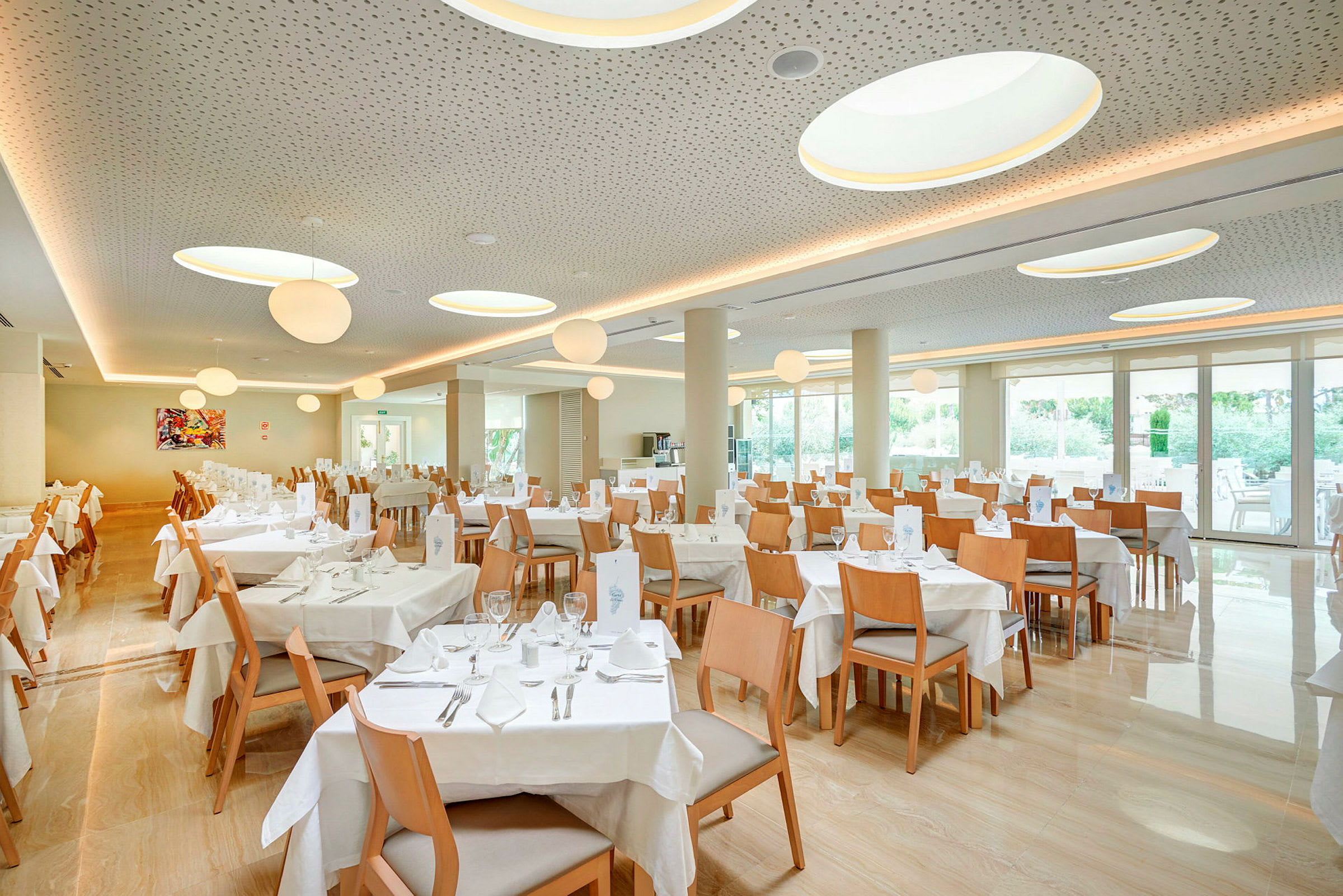 En restaurant med flere borde og træstole, store vinduer og loftslamper. (AI-genereret tekst)