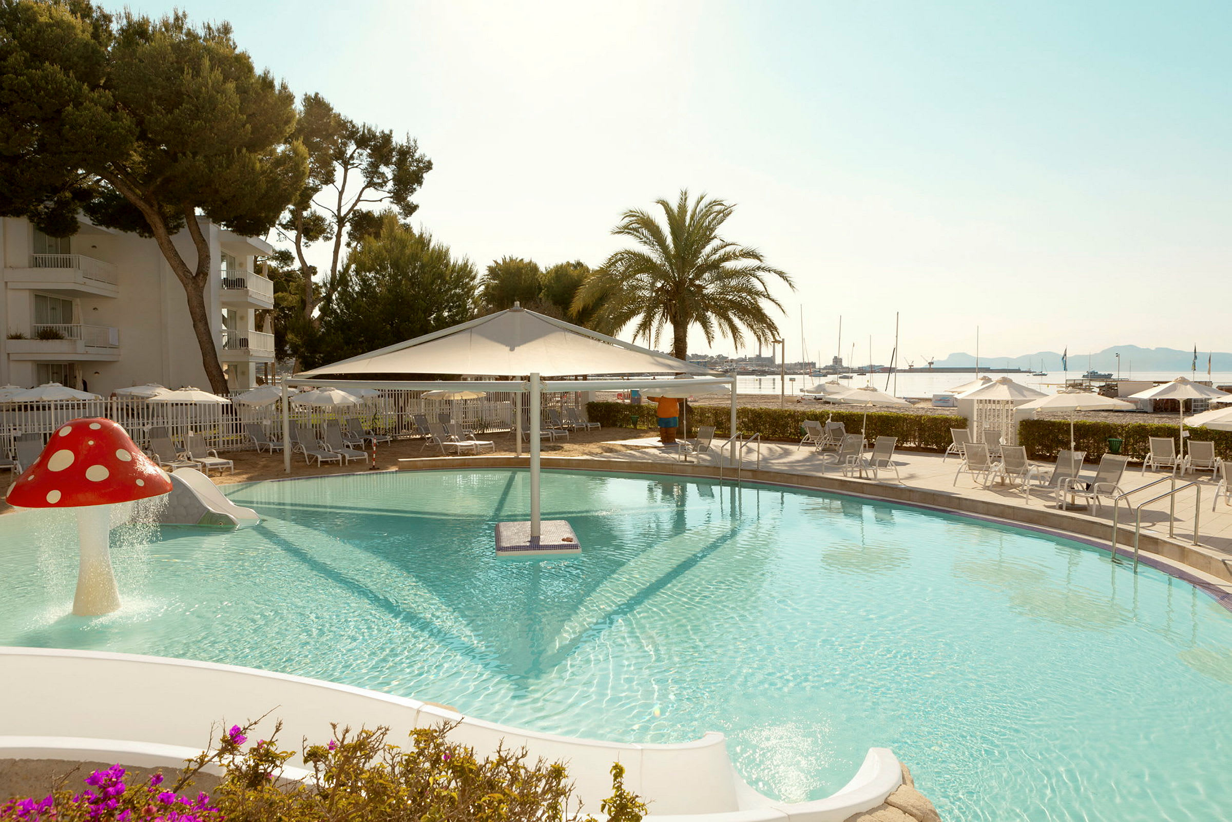 Pool med rutsjebaner og parasoller ved havet. (AI-genereret tekst)