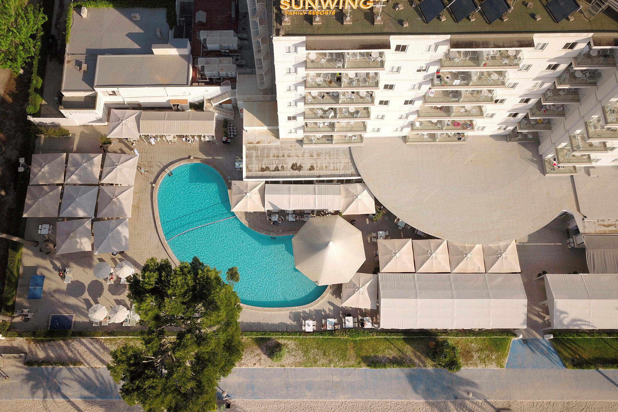 Luftfoto af hotelområde med pool, parasoller og bygninger. (AI-genereret tekst)