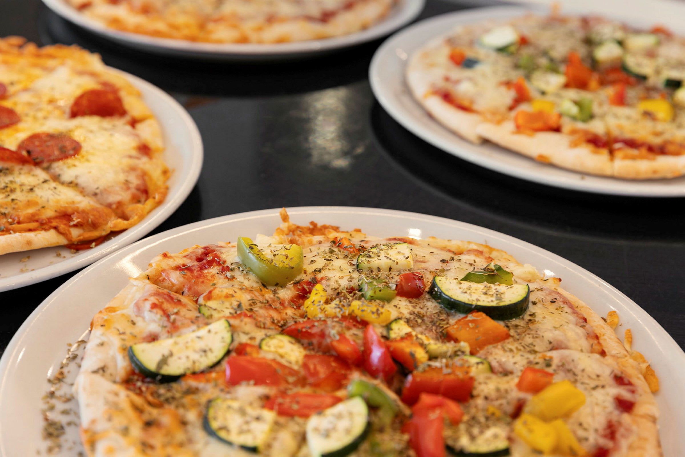 Fire pizzaer med forskellige toppings på tallerkener. (AI-genereret tekst)