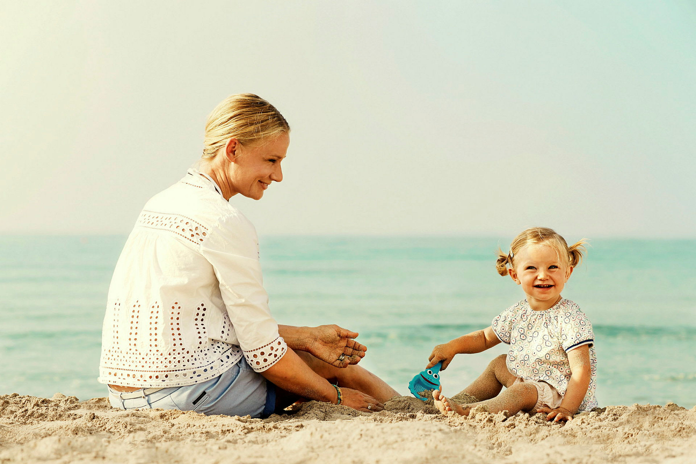 En person og et barn sidder på en sandstrand tæt ved vandet. (AI-genereret tekst)