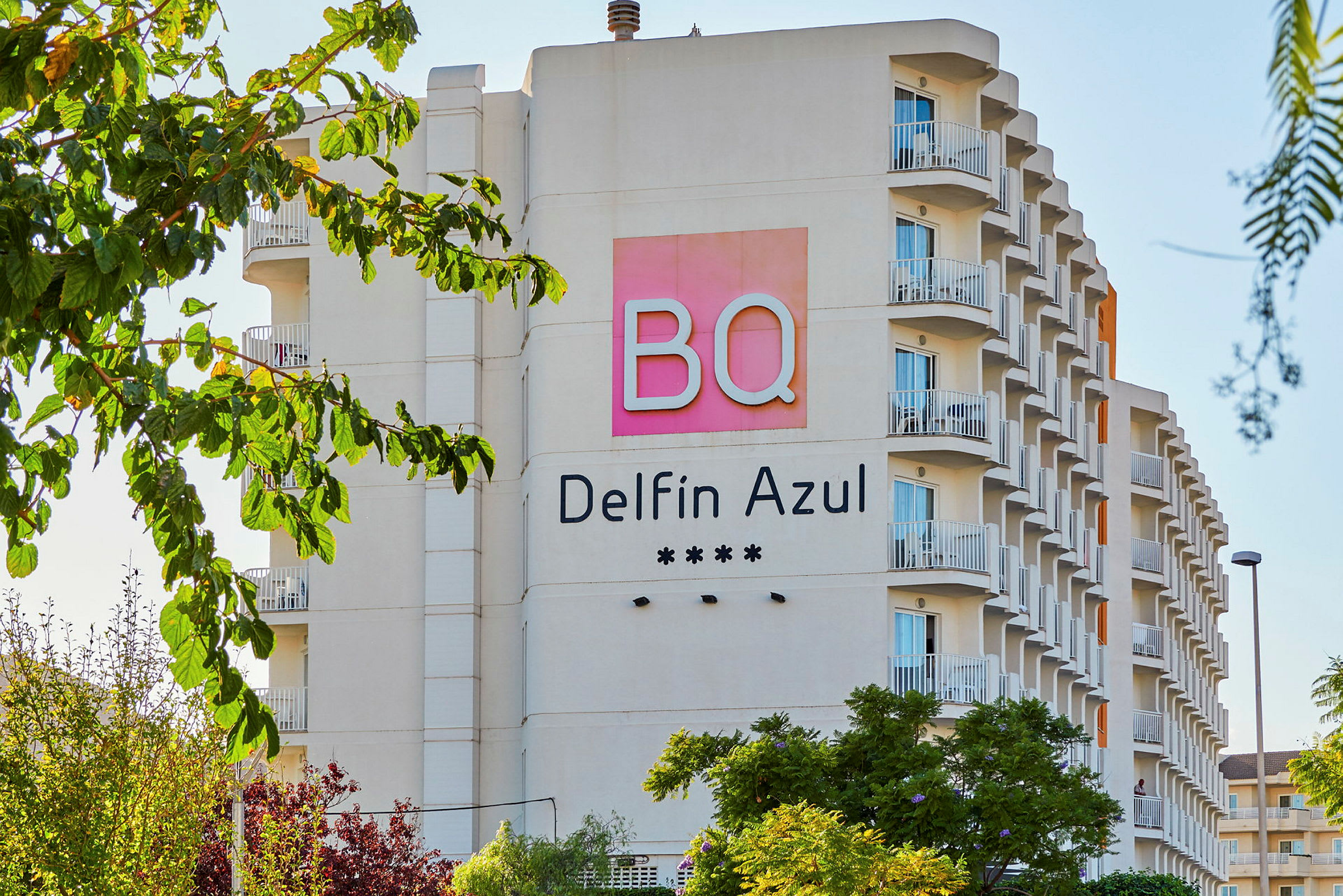 Hotellets facade med navnet BQ Delfin Azul og fire stjerner, omgivet af træer. (AI-genereret tekst)