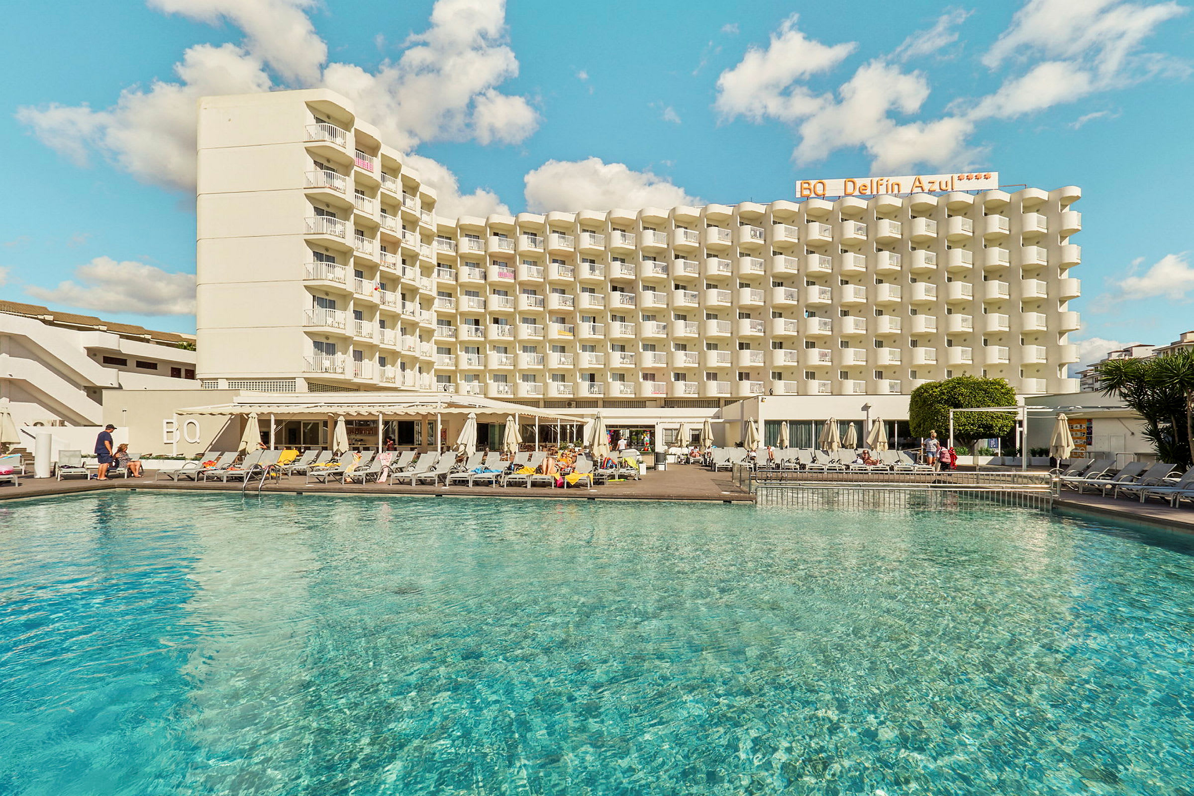 Billede af en hotelbygning med en pool i forgrunden. (AI-genereret tekst)