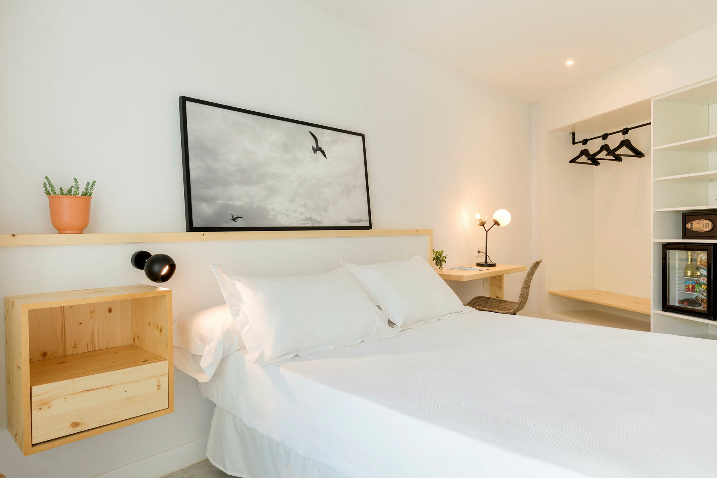 Et lyst hotelværelse med en hvid seng, trømøbler og vægdekoration. (AI-genereret tekst)