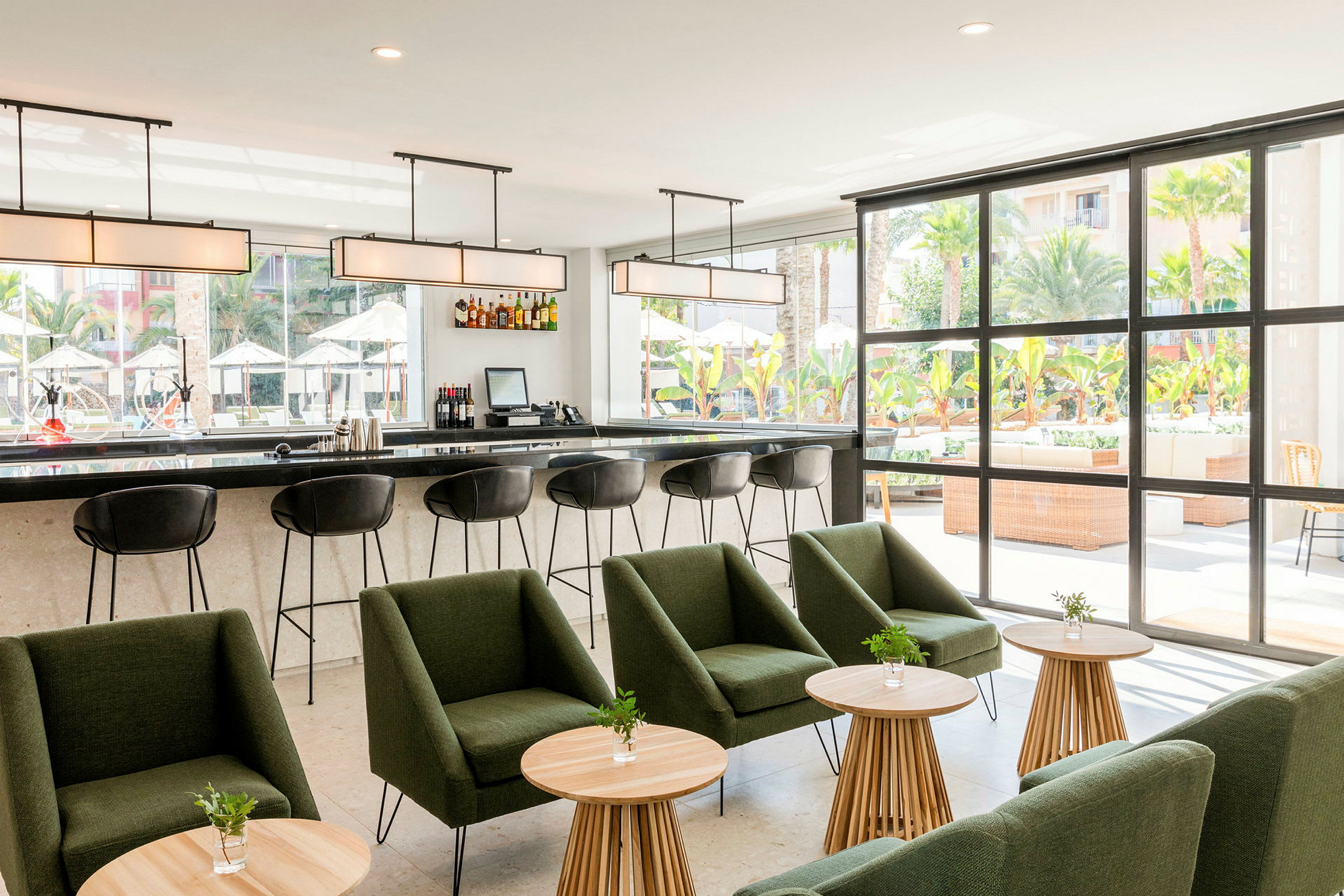 Moderne bar med stole og grøn siddegruppe foran store vinduer, der vender ud mod en udendørs terrasse. (AI-genereret tekst)