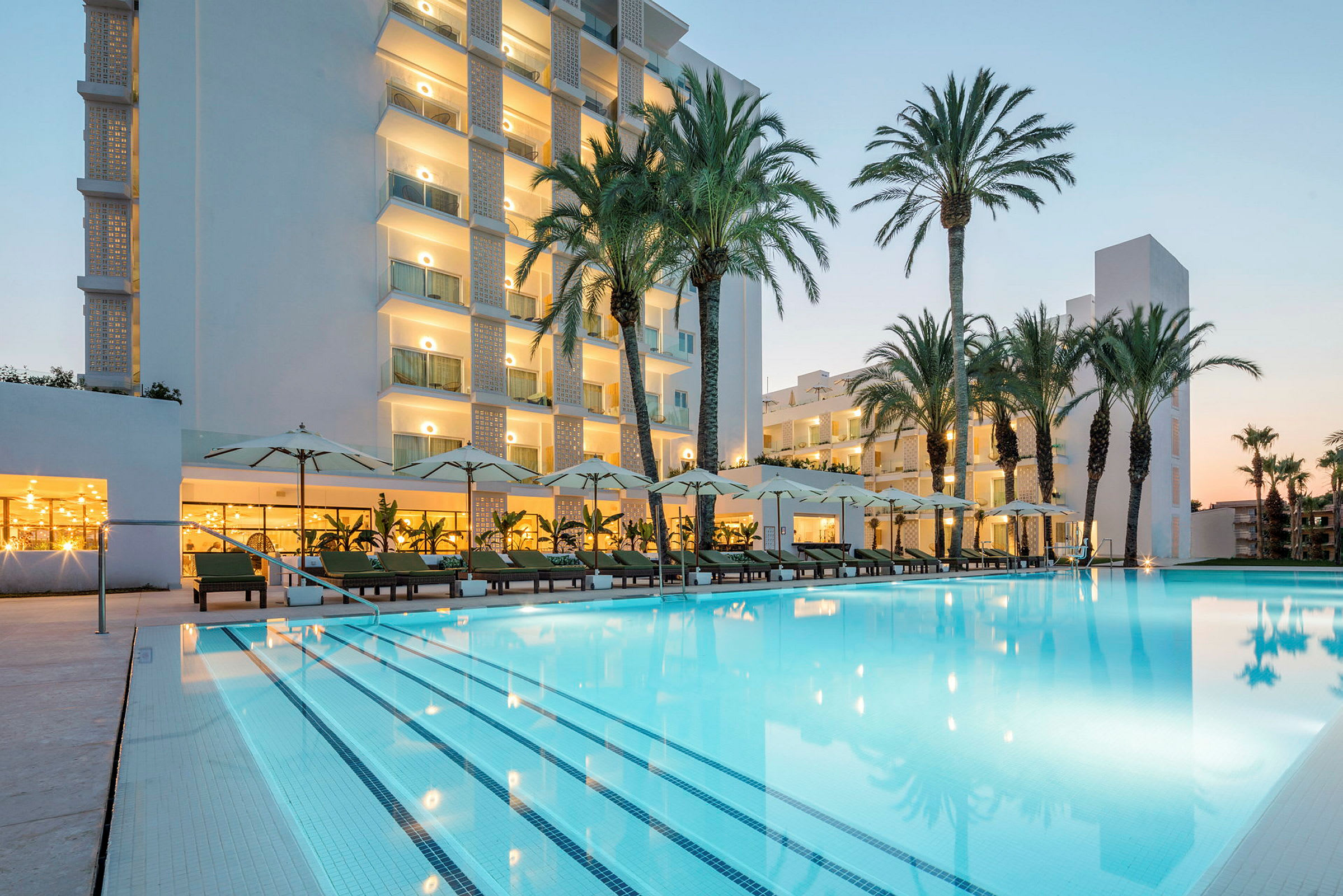 Hotel med pool og liggestole omgivet af palmer. (AI-genereret tekst)