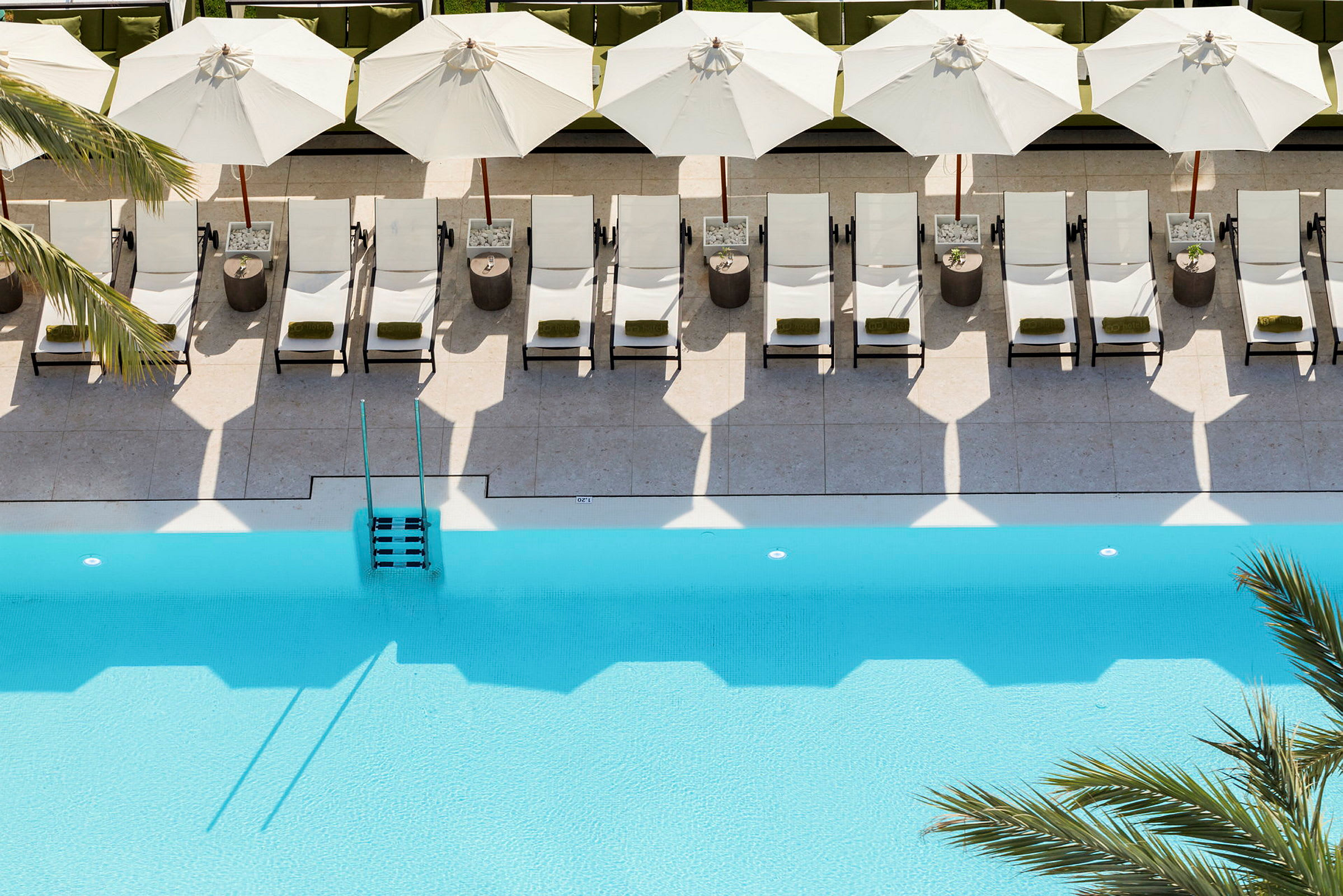 Liggestole og parasoller på en poolterrasse ved en blå pool. (AI-genereret tekst)