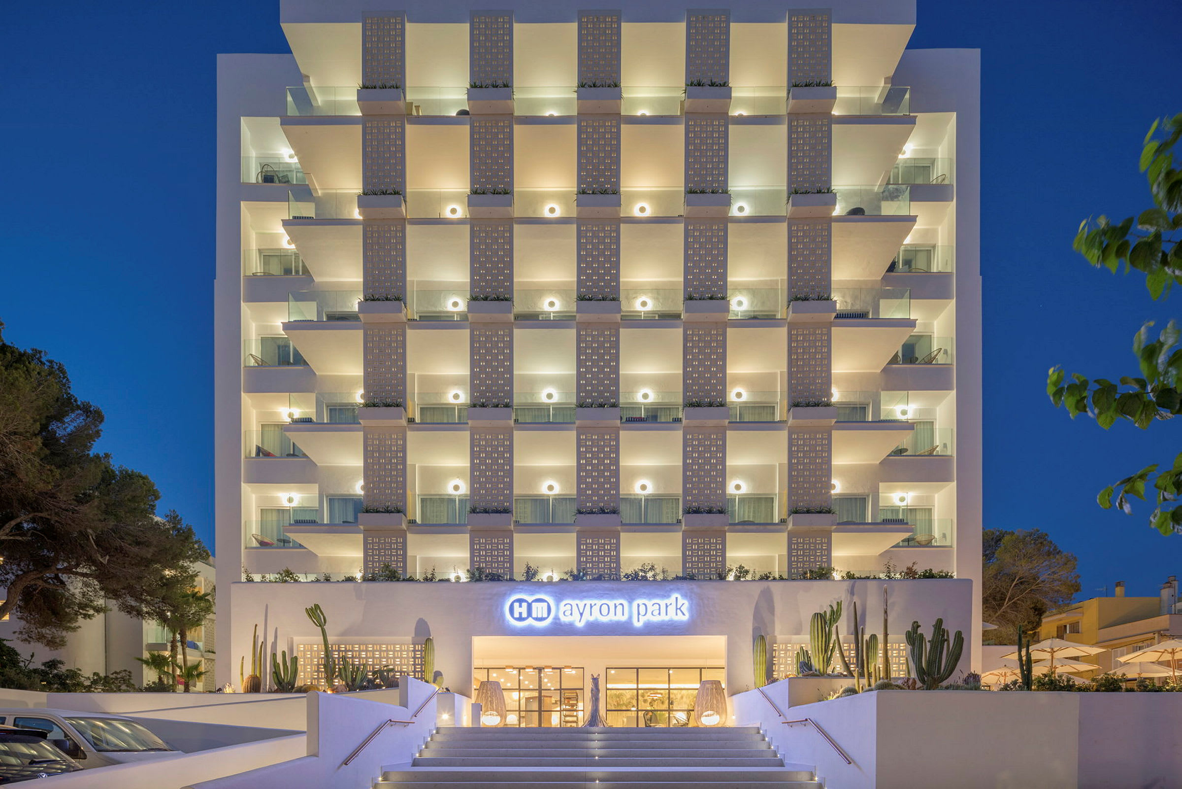 Hotel Ayron Parks facade om aftenen med oplyste altaner og hovedindgang. (AI-genereret tekst)