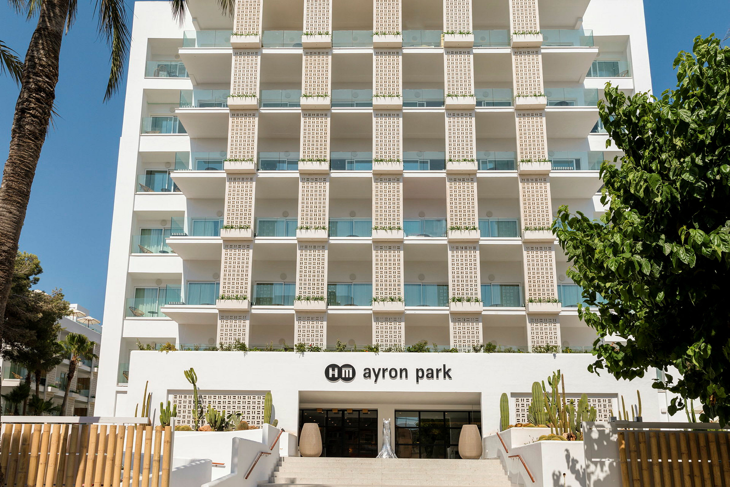Hotellets facade med altaner og indgangen til hm ayron park, dekoreret med kaktus. (AI-genereret tekst)