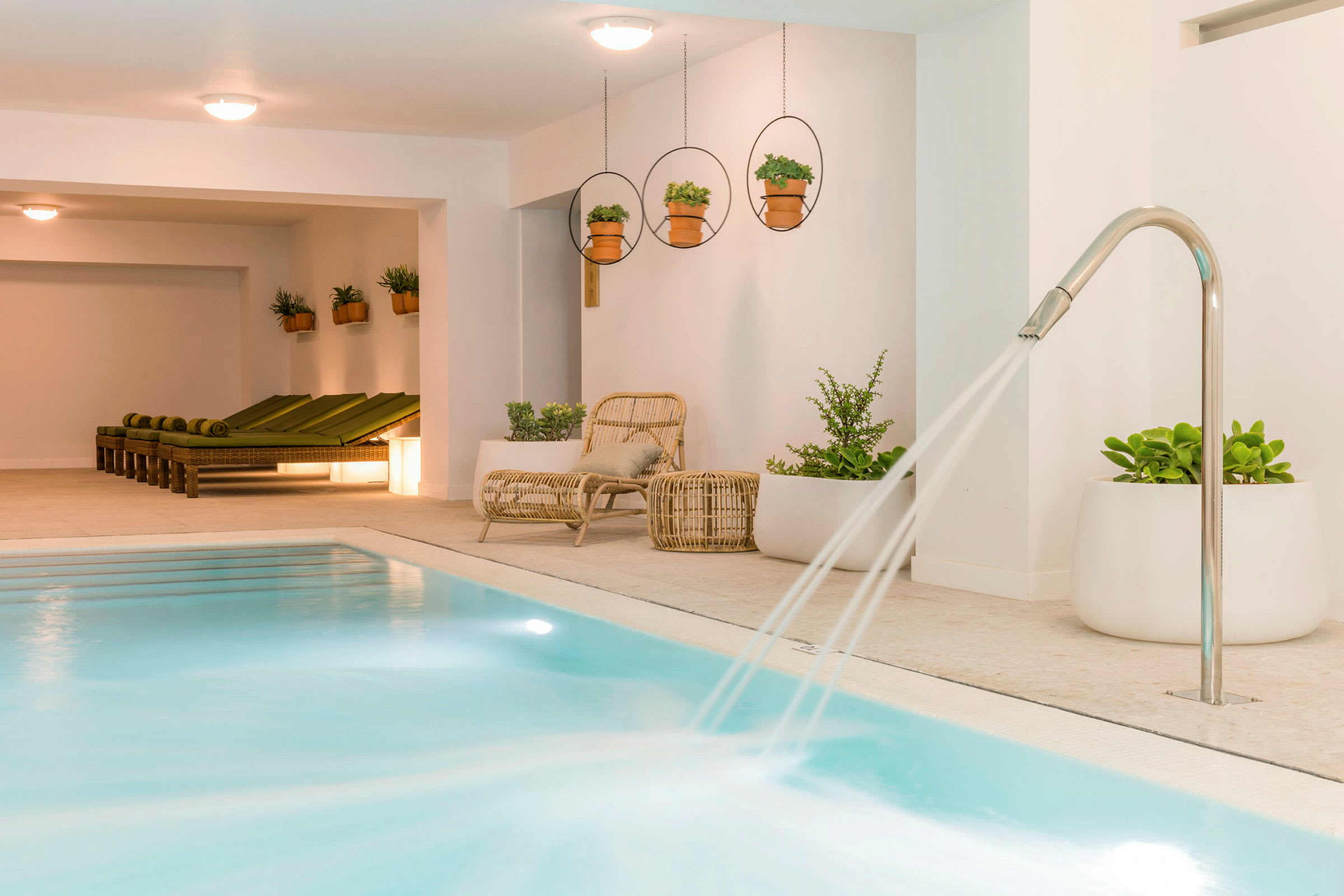 Indendørs pool med vandstråler og liggestole ved siden af planter. (AI-genereret tekst)
