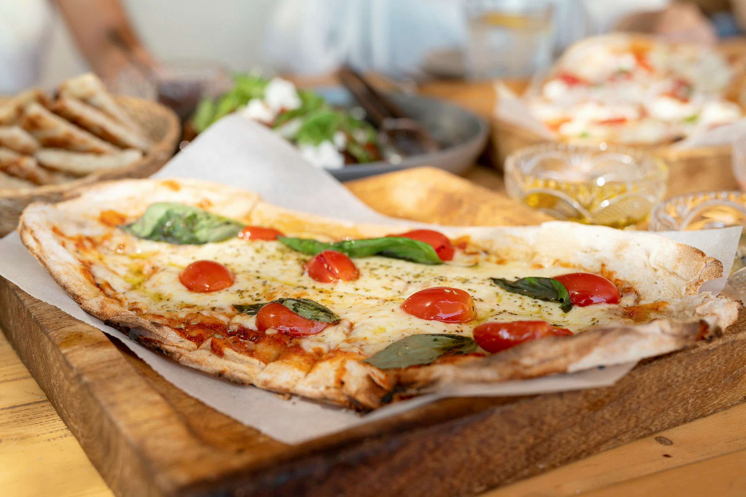 Firkantet pizza med tomater og basilikum på skærebræt af træ. (AI-genereret tekst)