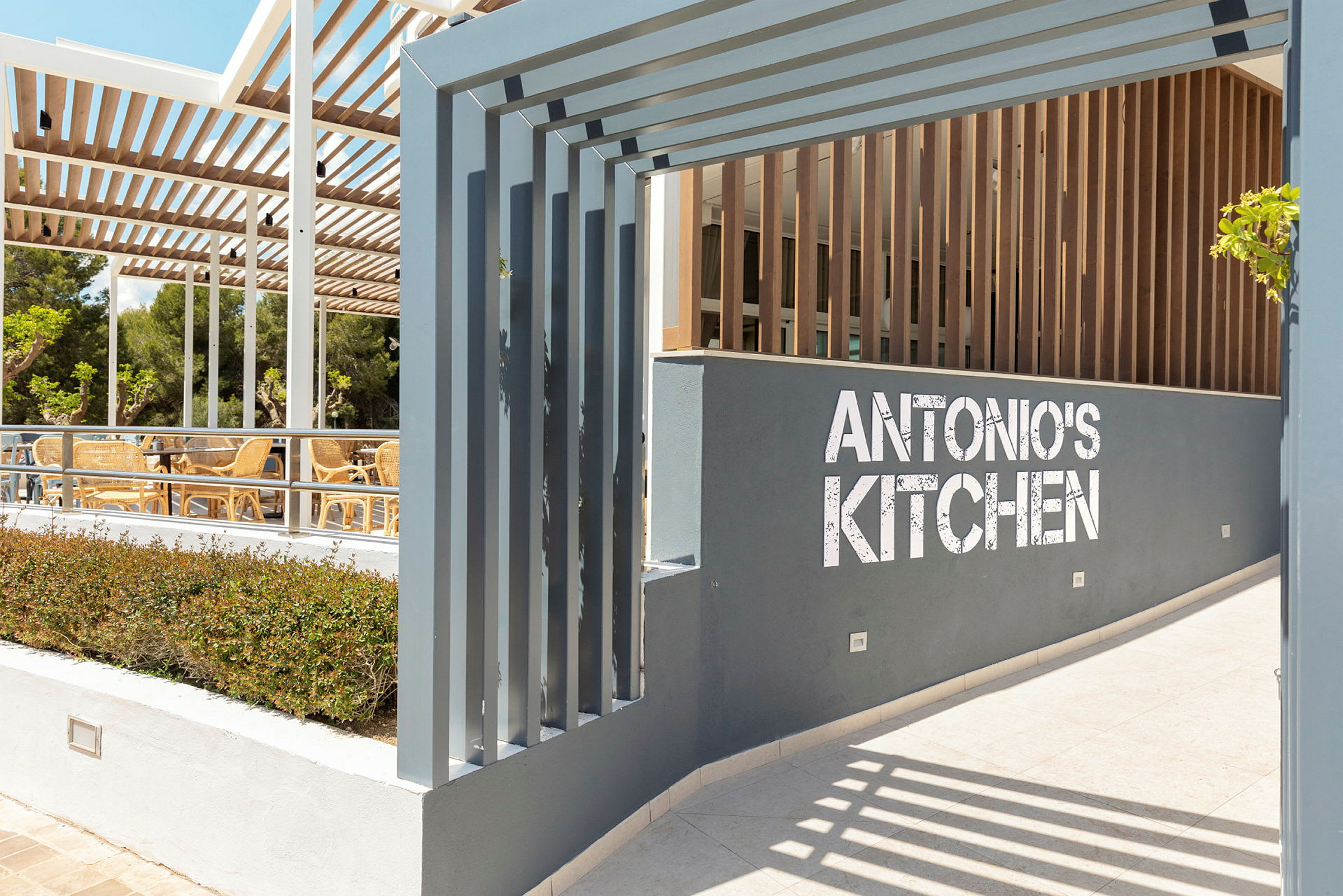 Indgang til restauranten Antonio's Kitchen med udendørs siddepladser. (AI-genereret tekst)