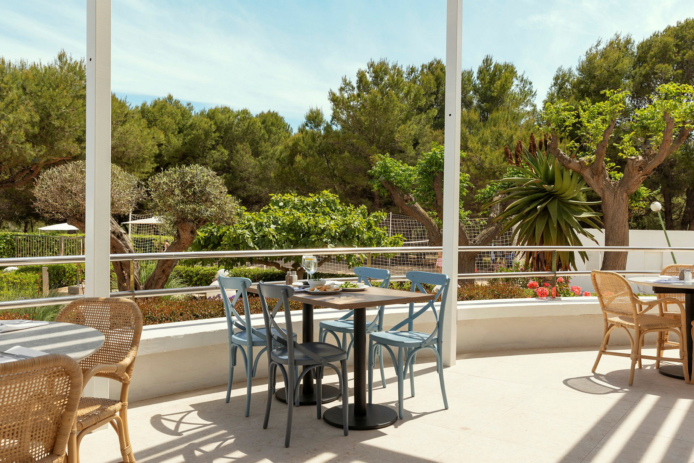 En åben siddegruppe med borde og stole på en terrasse, omgivet af grønne områder. (AI-genereret tekst)