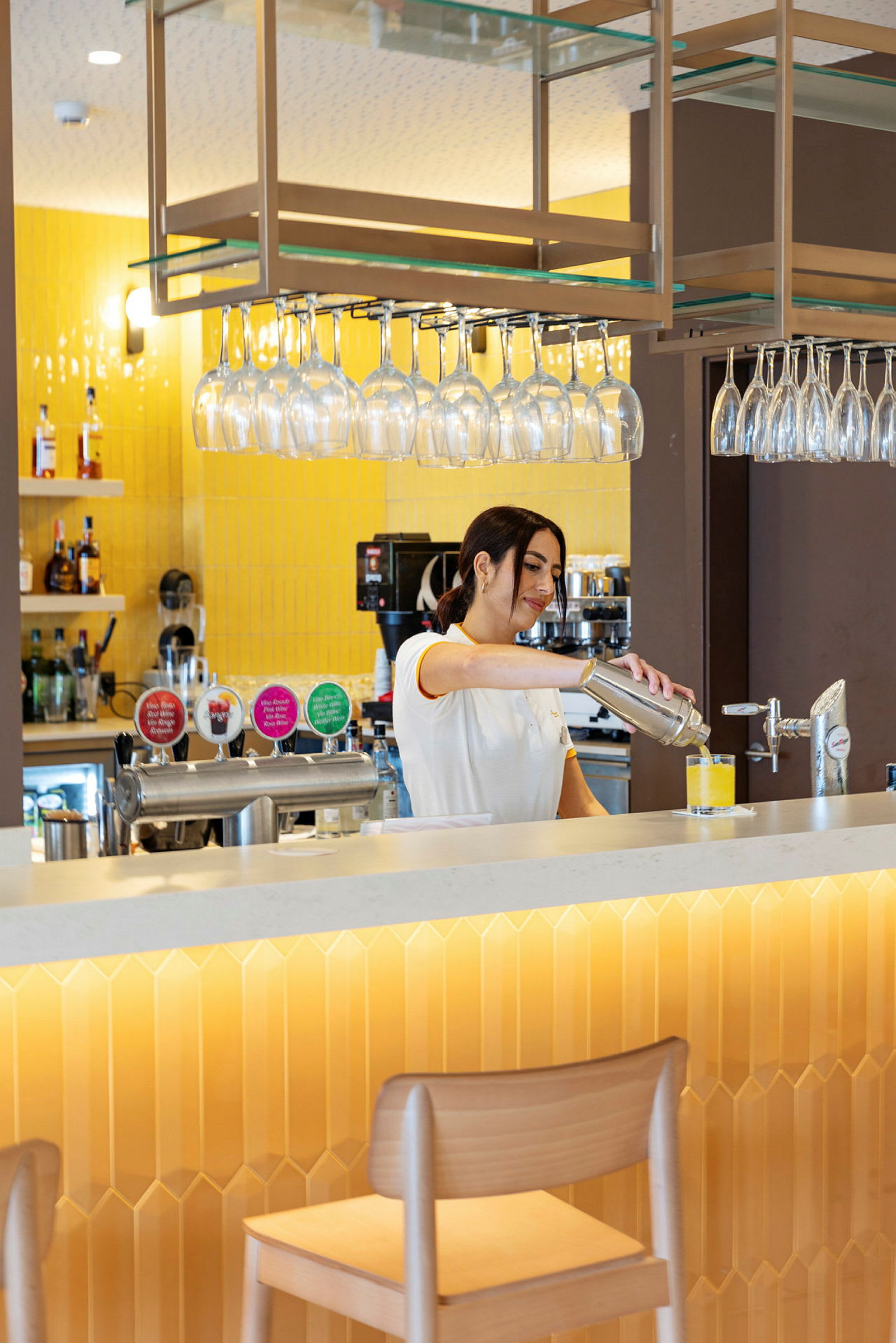 Personen forbereder en drink ved en bar med gul indretning. (AI-genereret tekst)