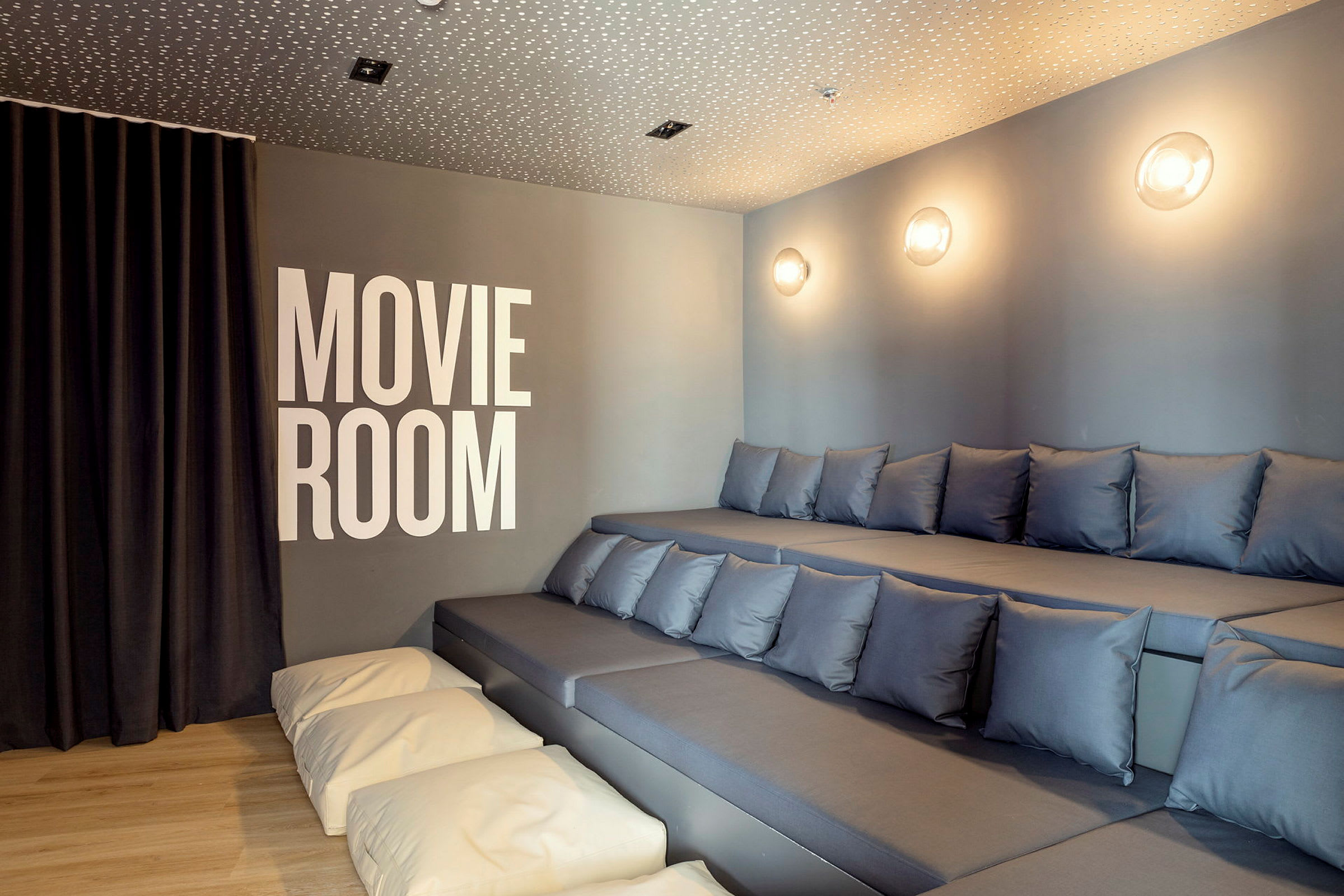 Billede af et filmrum med graduerede siddepladser med puder og teksten 'Movie Room' på væggen. (AI-genereret tekst)