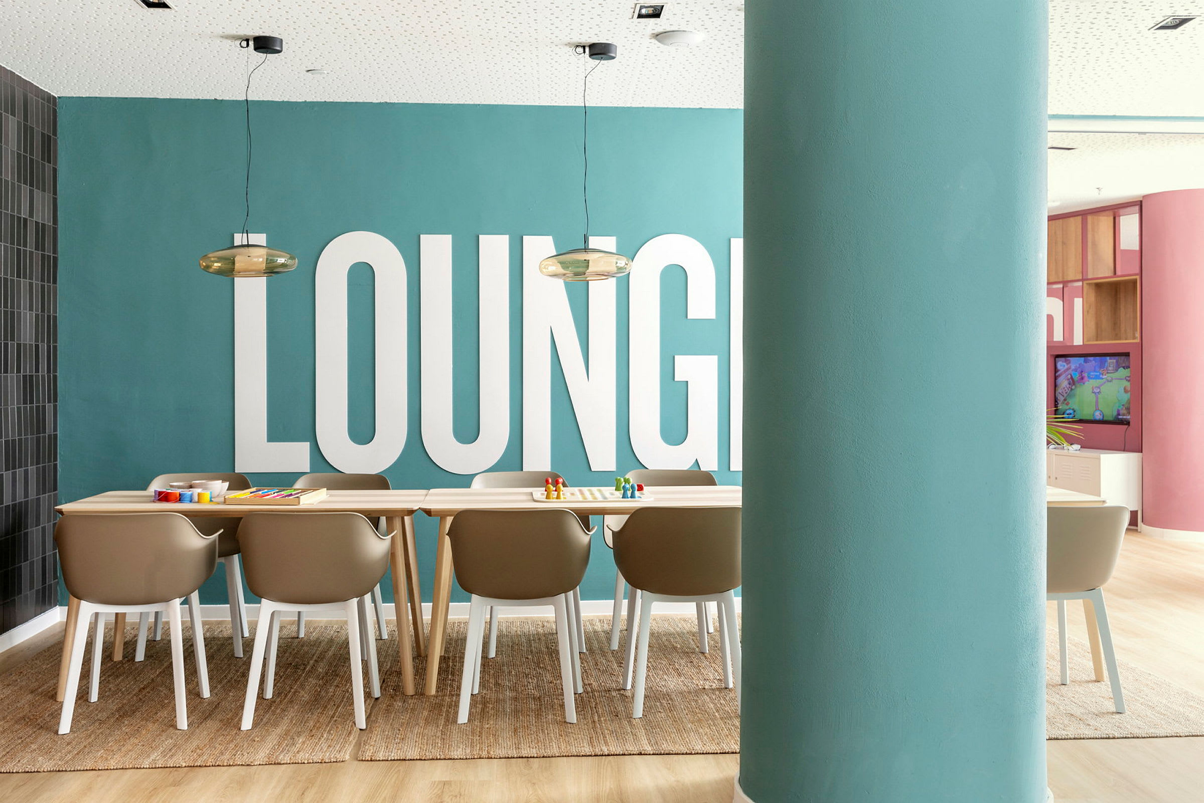 Et billede af et rum med et tæppe, stole og et bord foran en blå væg med teksten 'LOUNGE'. (AI-genereret tekst)