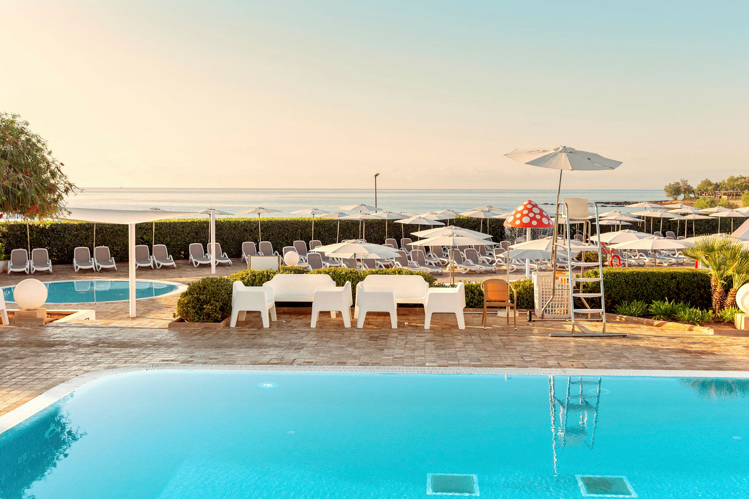 En swimmingpool med liggestole og parasoller på en solrig terrasse nær havet. (AI-genereret tekst)