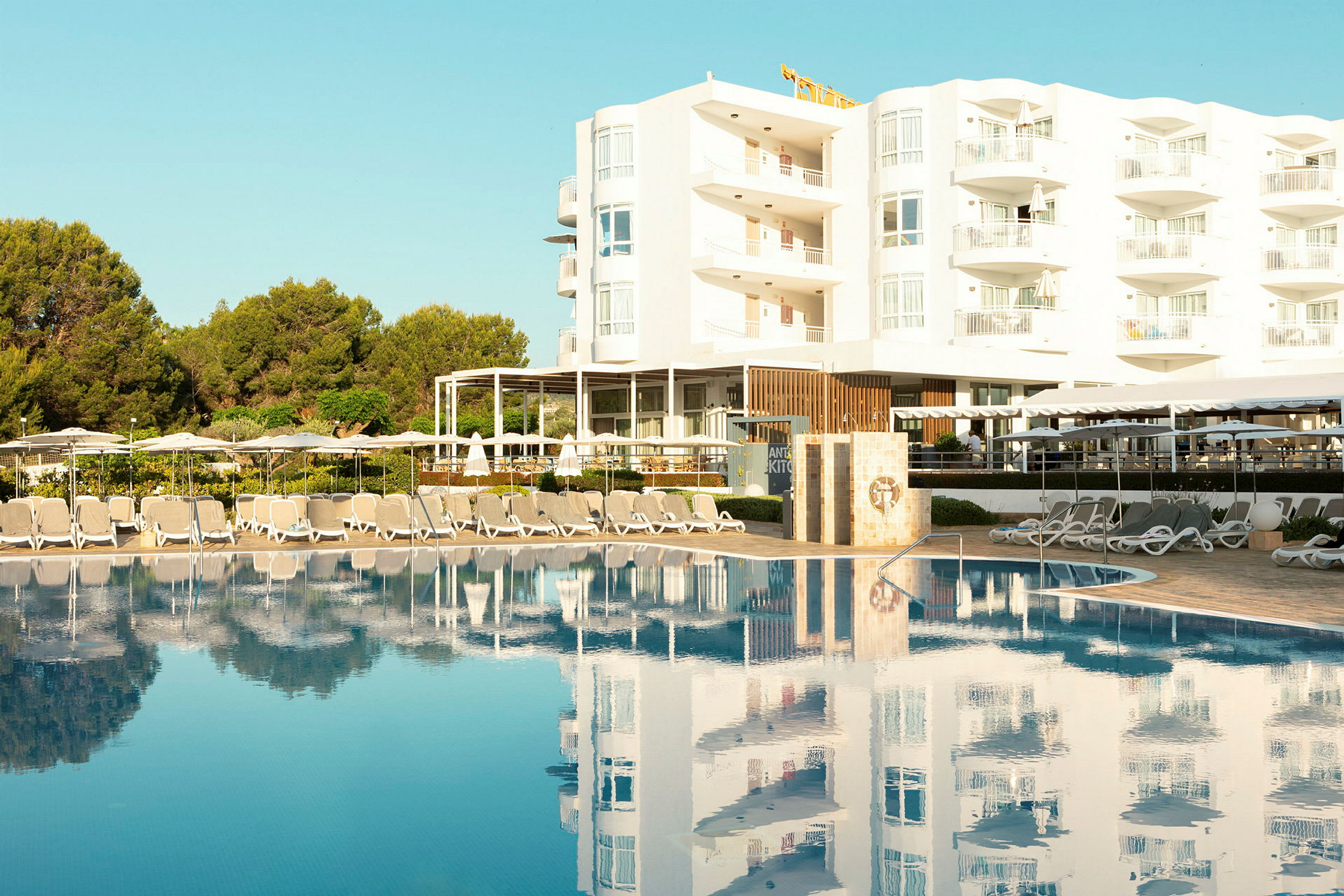 Liggestole og parasoller ved en pool foran et hotel. (AI-genereret tekst)