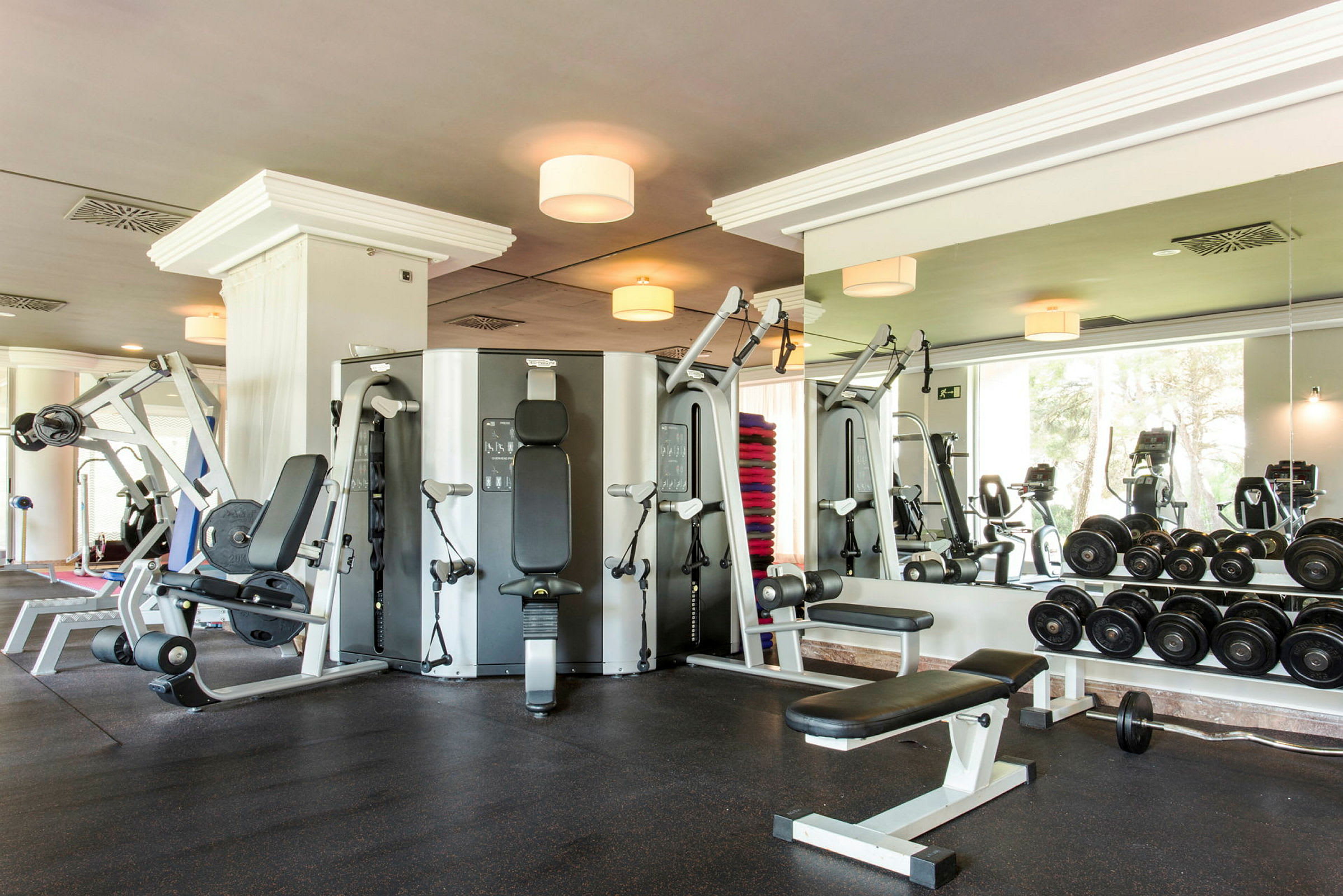 Et fitnesscenter med forskellige træningsmaskiner, håndvægte og et spejl på væggen. (AI-genereret tekst)