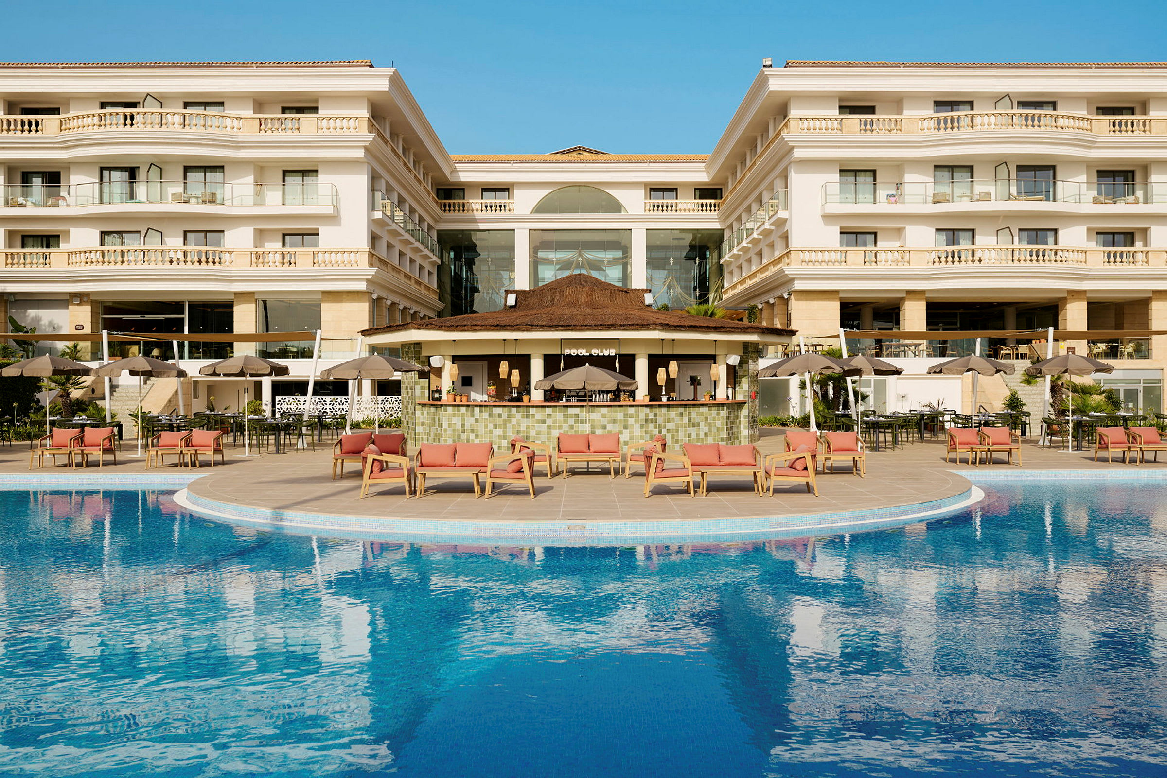 Hotelbygning med en pool og afslapningsområder udenfor. (AI-genereret tekst)