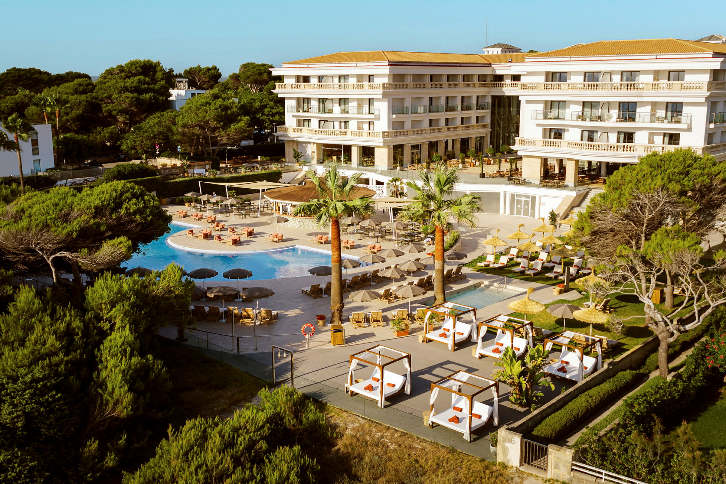 Et hotel med en stor udendørs pool og solsenge omgivet af grønne områder. (AI-genereret tekst)