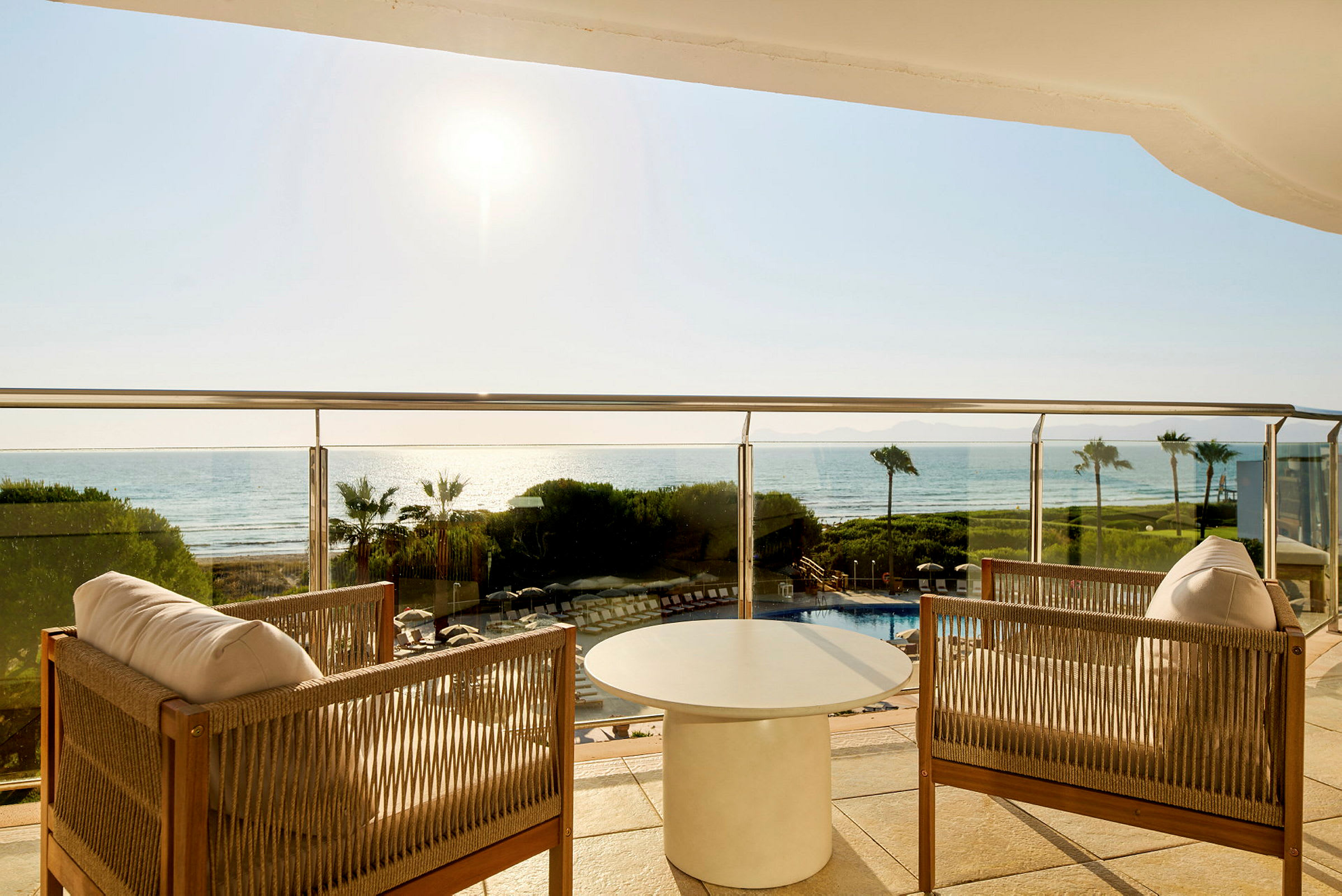 To stole og et bord på en balkon med udsigt over havet og solskin. (AI-genereret tekst)