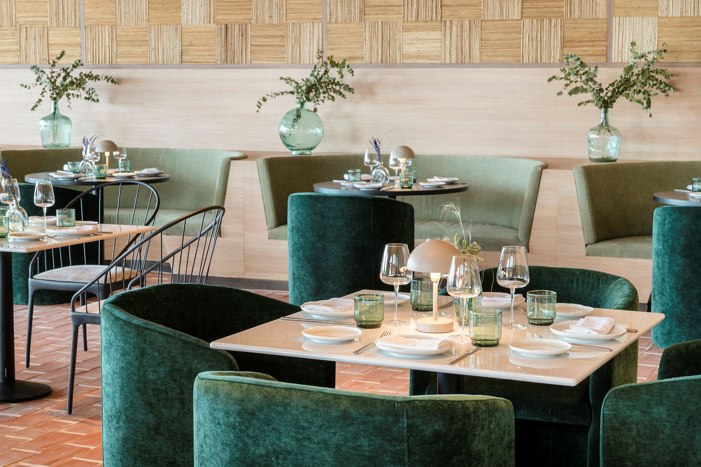 Et elegant indrettet restaurantområde med grøn polstring, dækkede borde og dekorative vaser med planter. (AI-genereret tekst)