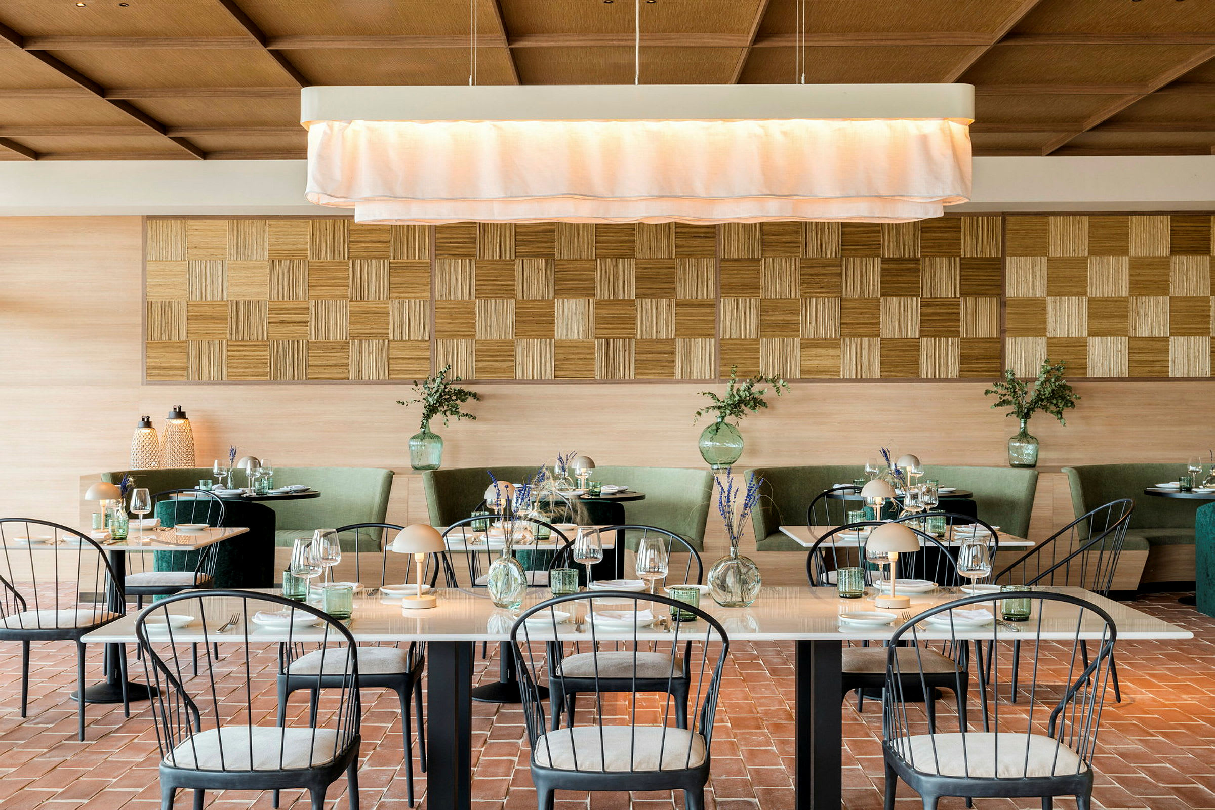En elegant restaurant med pænt dækkede borde, grønne sofaer og en lys indretning. (AI-genereret tekst)