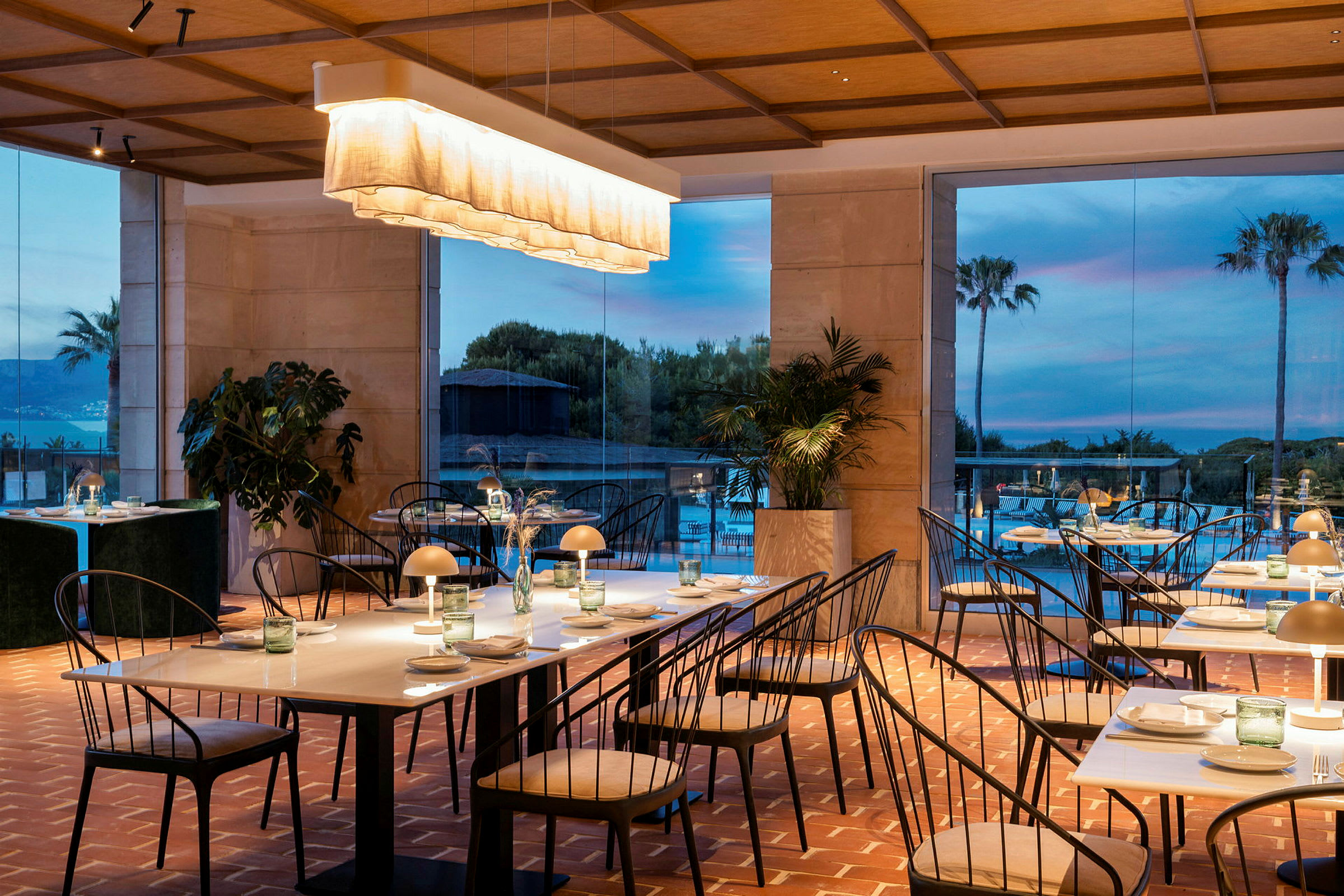 En elegant indrettet restaurant med borde og stole samt en lys indretning. I baggrunden ses store vinduer med en naturskøn udsigt. (AI-genereret tekst)