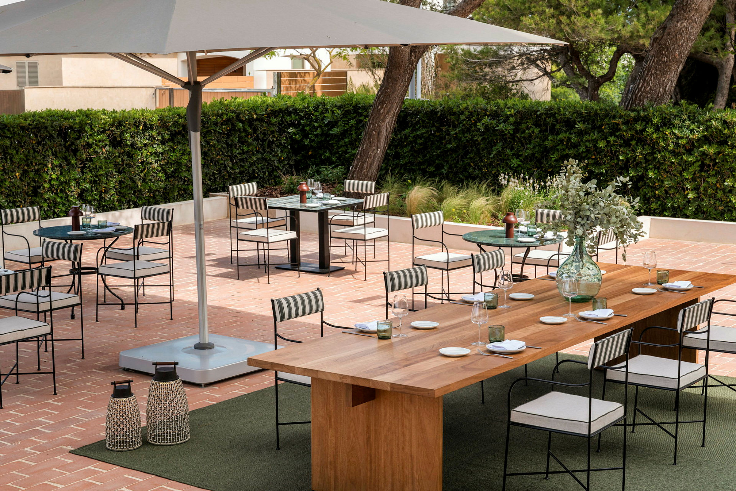 Udendørs serveringsområde med borde og stole på en terrasse omgivet af grønne områder. (AI-genereret tekst)
